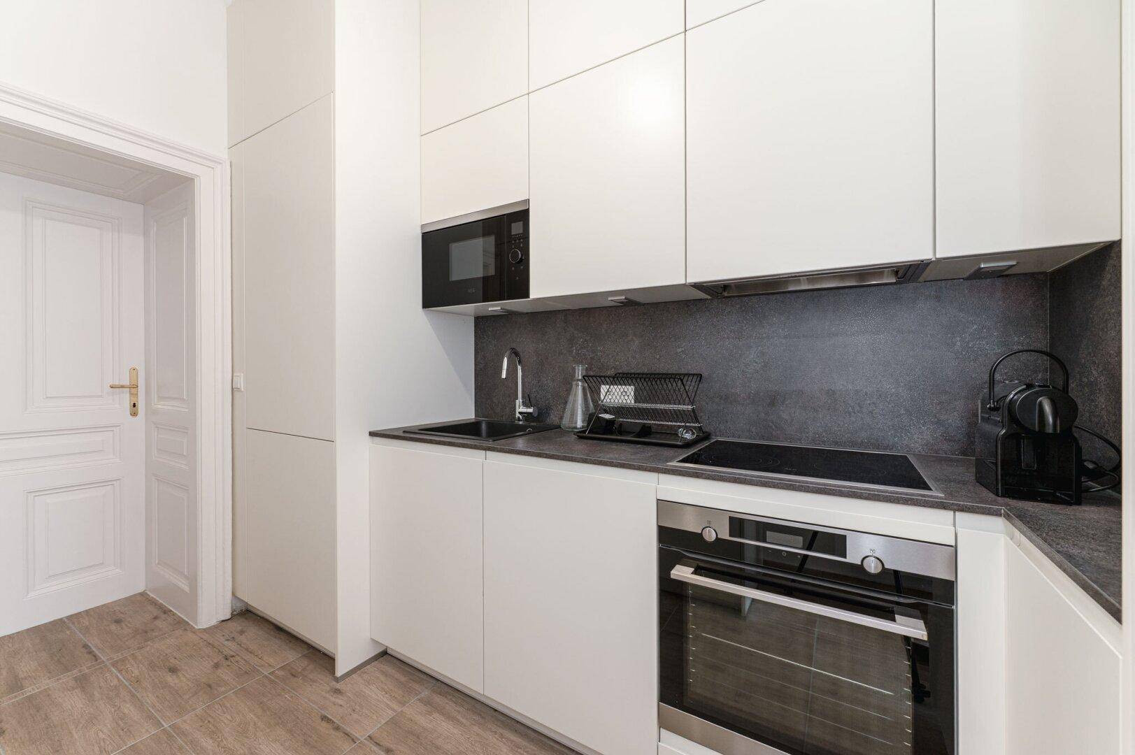 Moderne Einbauküche mit weißen Schränken, dunkler Arbeitsplatte und integrierten Geräten.