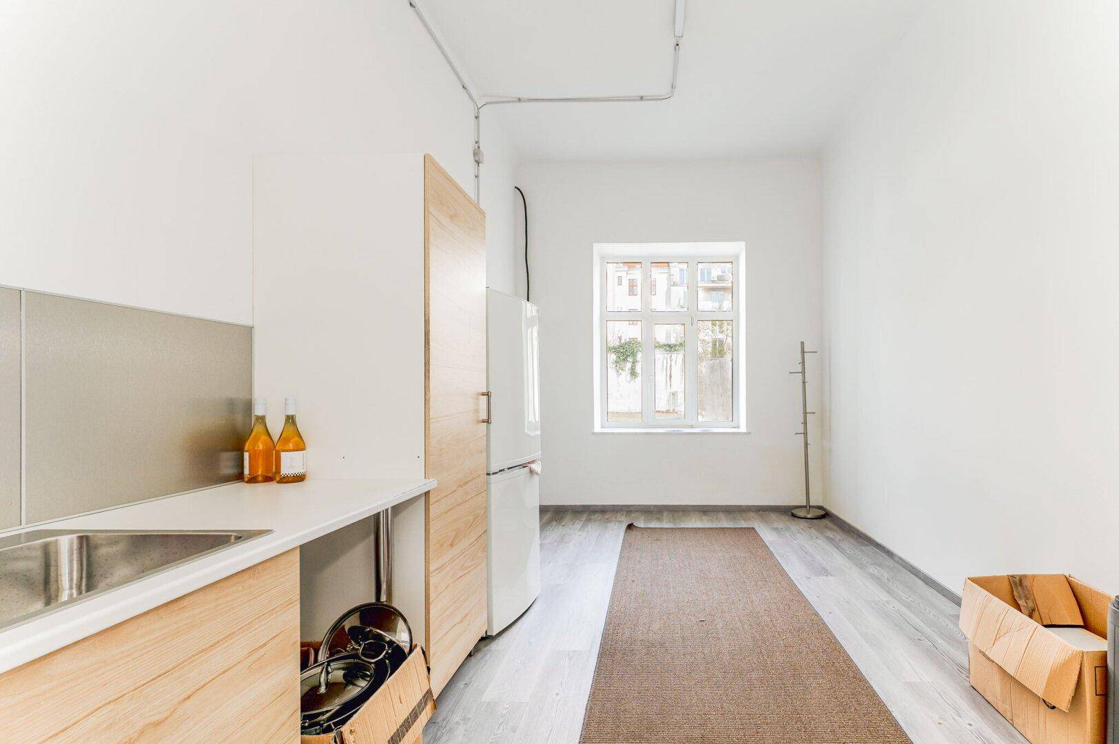 Kleine Küchenzeile mit Spüle, Kühlschrank und Fenster in einem hellen, funktionalen Raum.