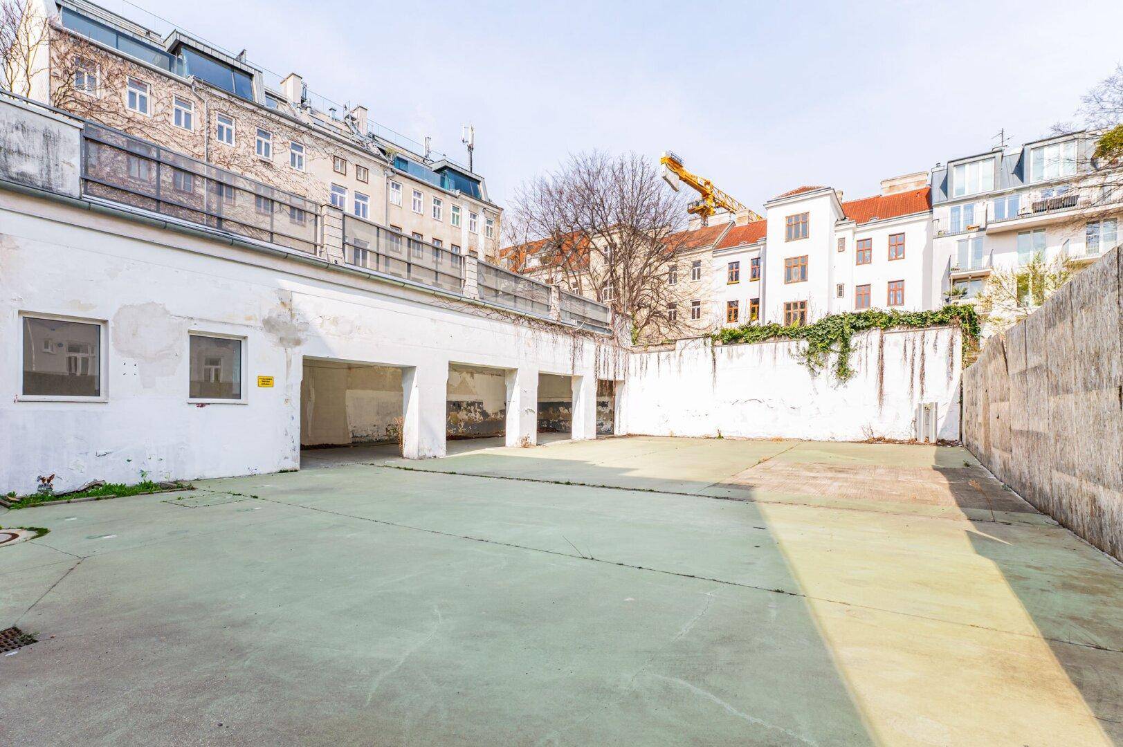 Hinterhof mit Garagen und einer großen, gepflasterten Fläche, umgeben von Altbauten.