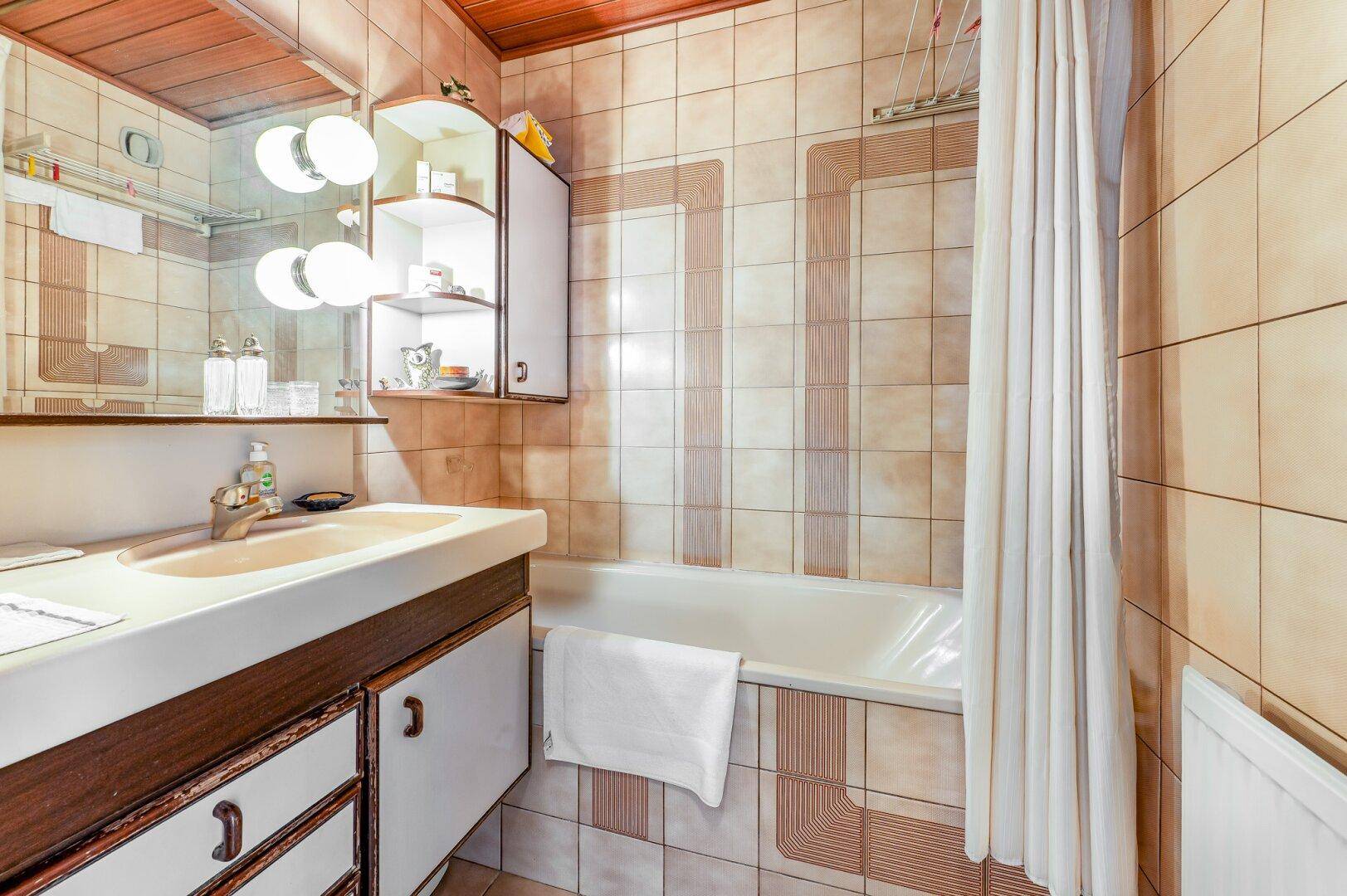 Badezimmer mit beigefarbenen Fliesen, Badewanne und einem Waschbecken mit Spiegelschrank.