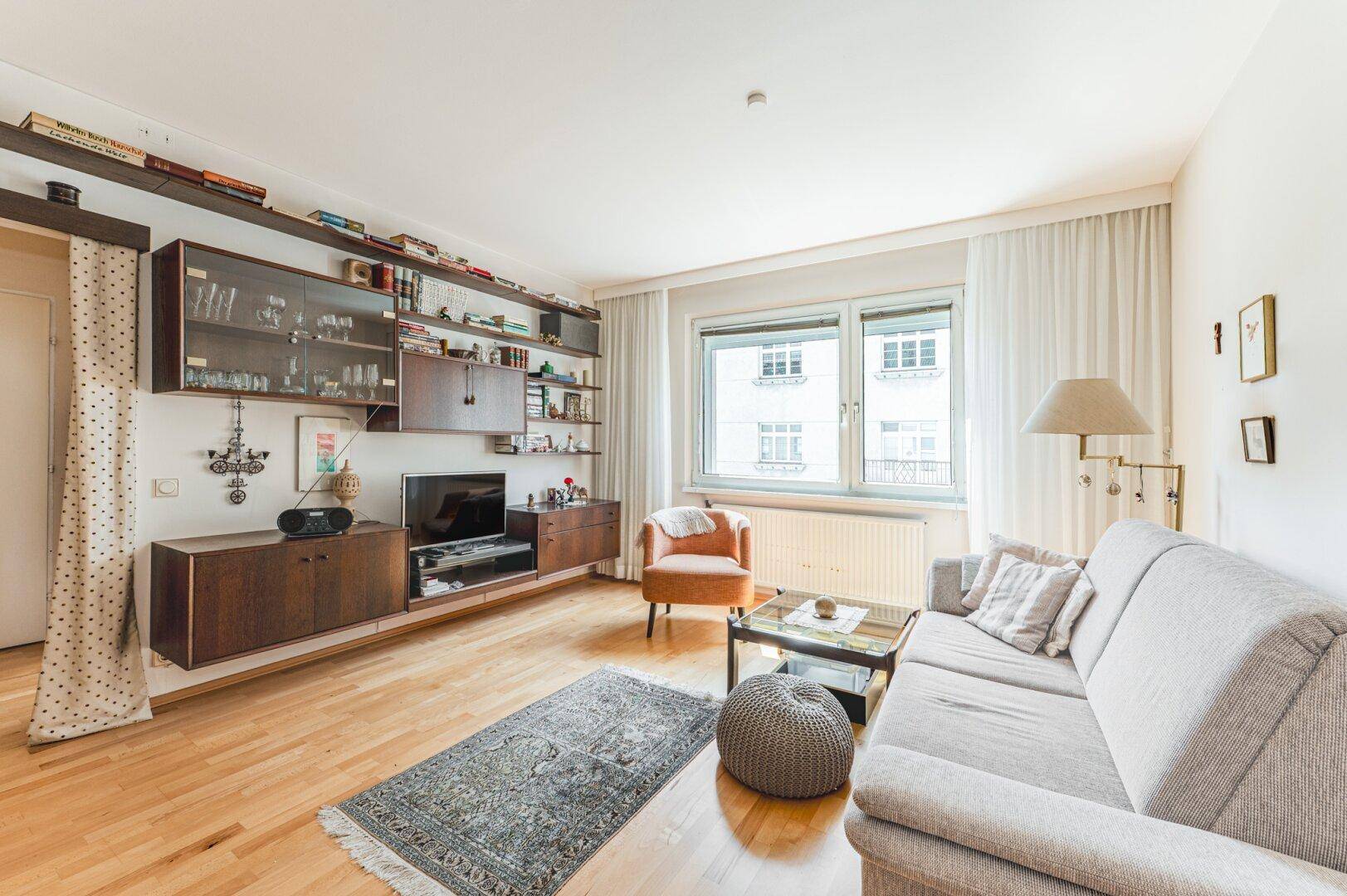 Helles Wohnzimmer mit Holzfußboden, einem Sofa und einem großen Fenster mit Vorhängen.