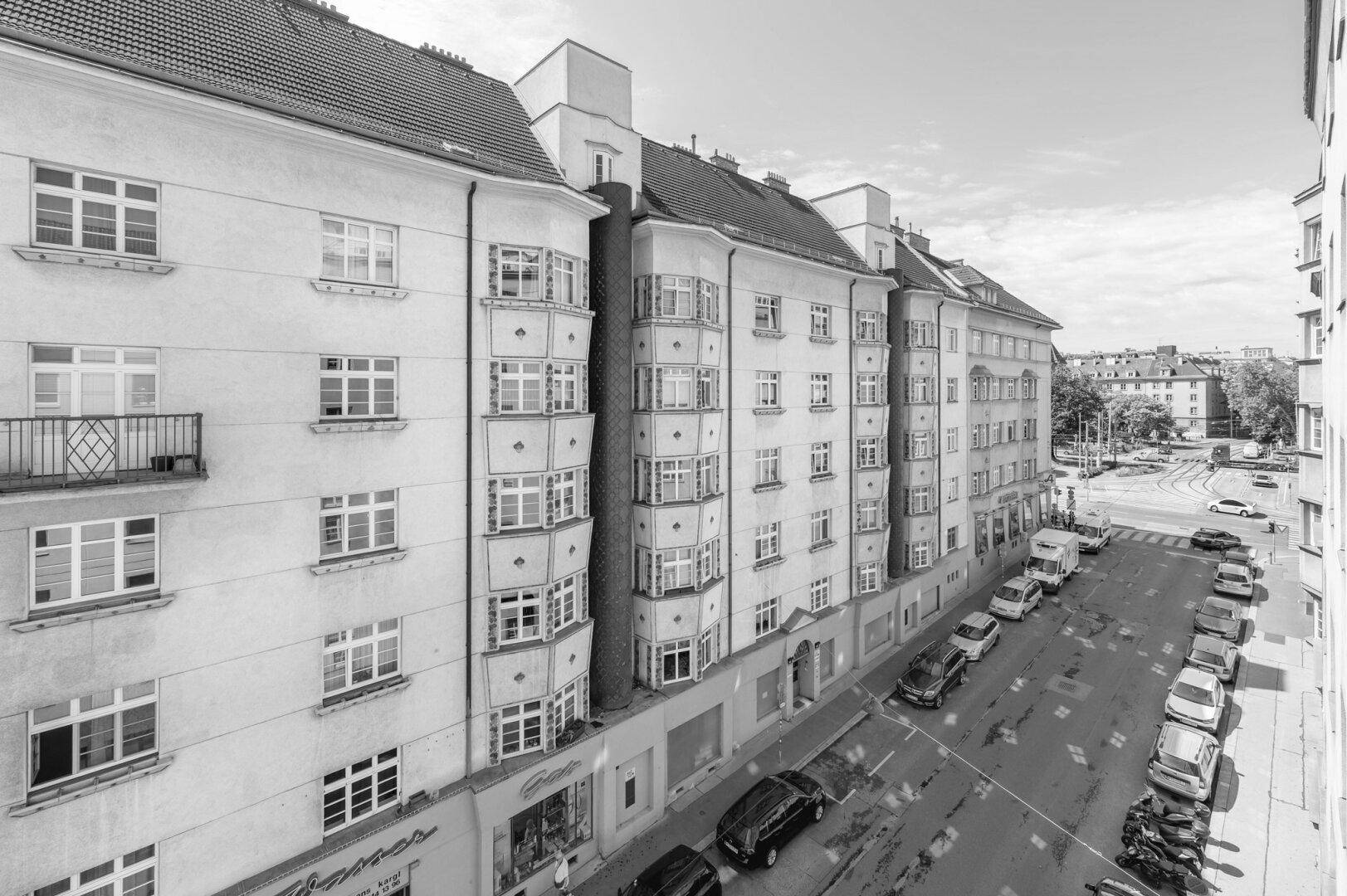 Schwarz-Weiß-Aufnahme einer belebten Straße mit parkenden Autos und einem Wohngebäude.
