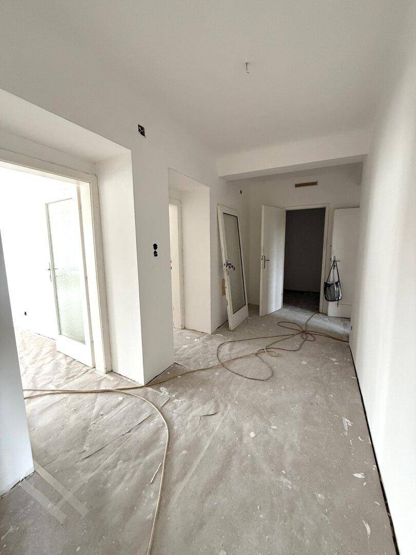 Langer Flur in Renovierung mit weißen Wänden, mehreren Türen und abgedecktem Boden.