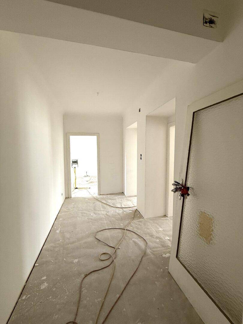 Heller Flur in Renovierung mit weißen Wänden, offenen Durchgängen und einer Tür mit Milchglas.