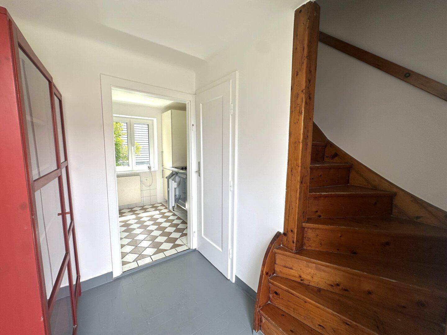 Flur mit rustikaler Holztreppe und Blick in die angrenzende kleine Küche.
