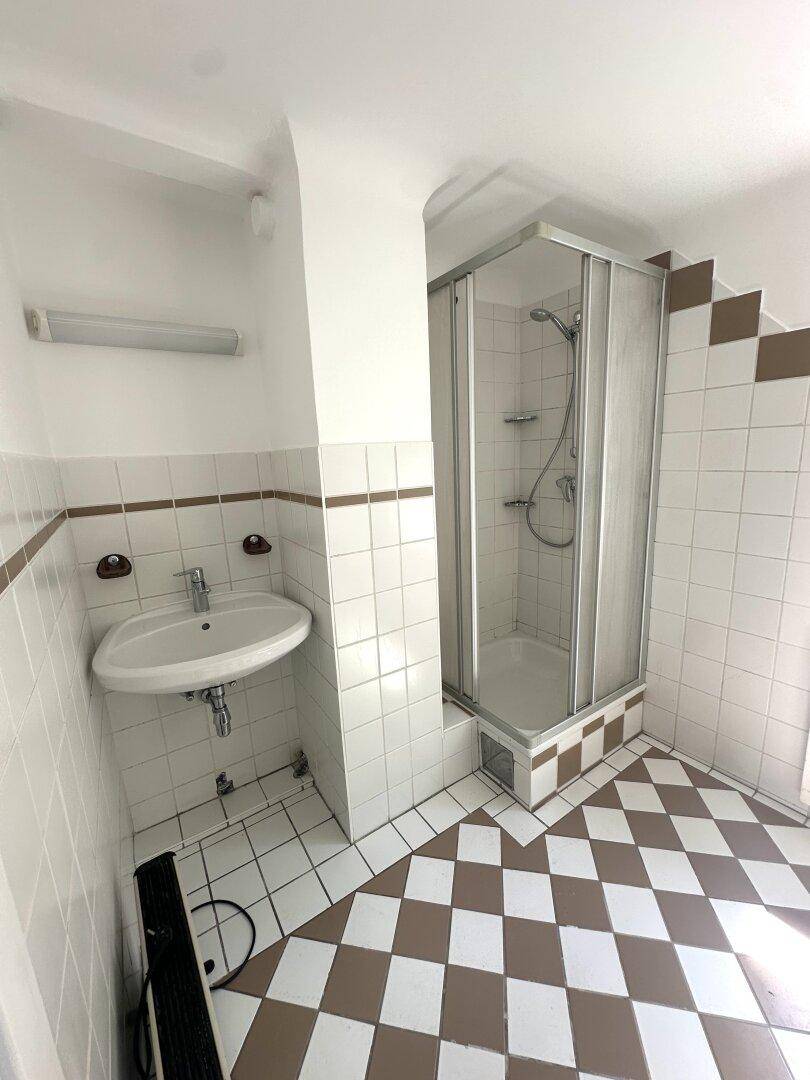 Badezimmer mit Duschkabine, Waschbecken und auffälligen braun-weißen Fliesen.