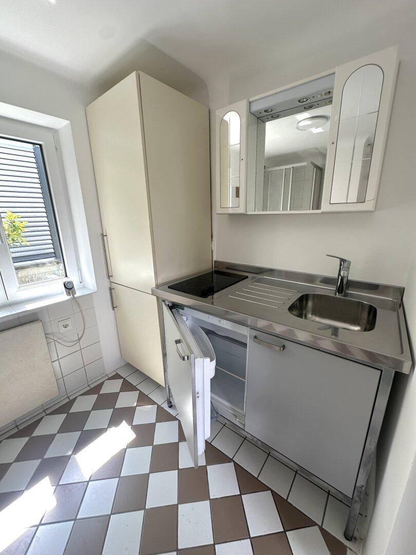 Kleine Küche mit kompakter Küchenzeile, Kühlschrank und Fenster.