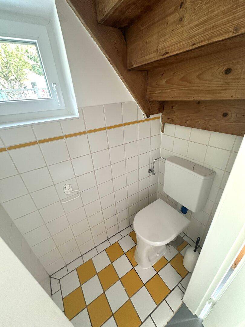 Kleines WC unter der Treppe mit gelb-weiß karierten Fliesen und Fenster.