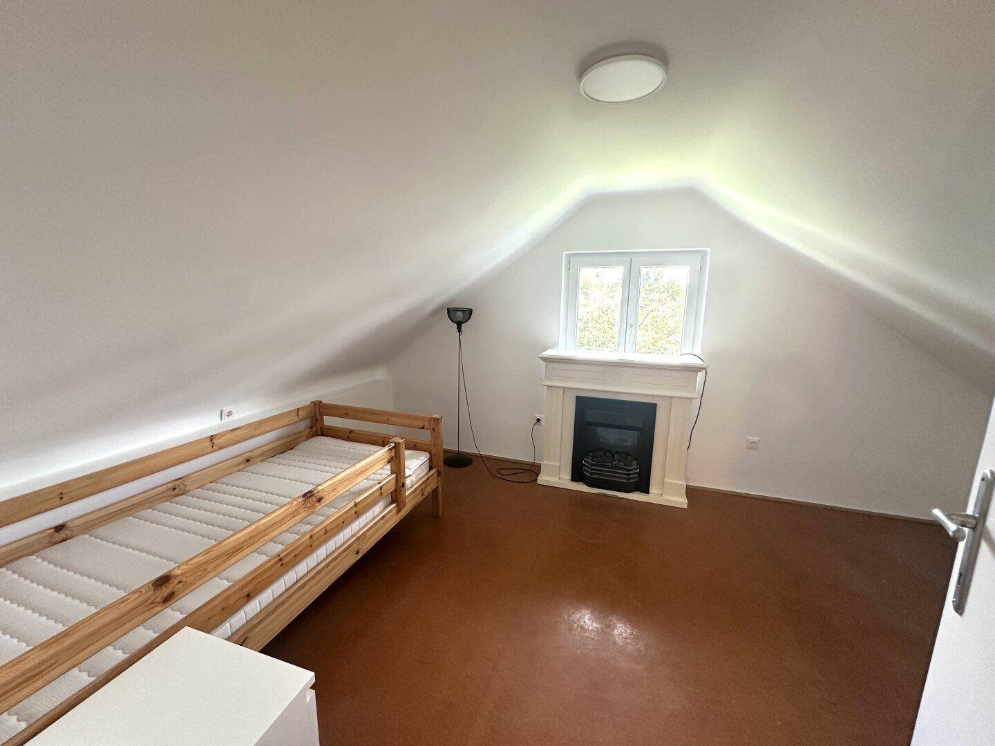 Schlafzimmer im Dachgeschoss mit Einzelbett, dekorativem Kamin und Dachschräge.