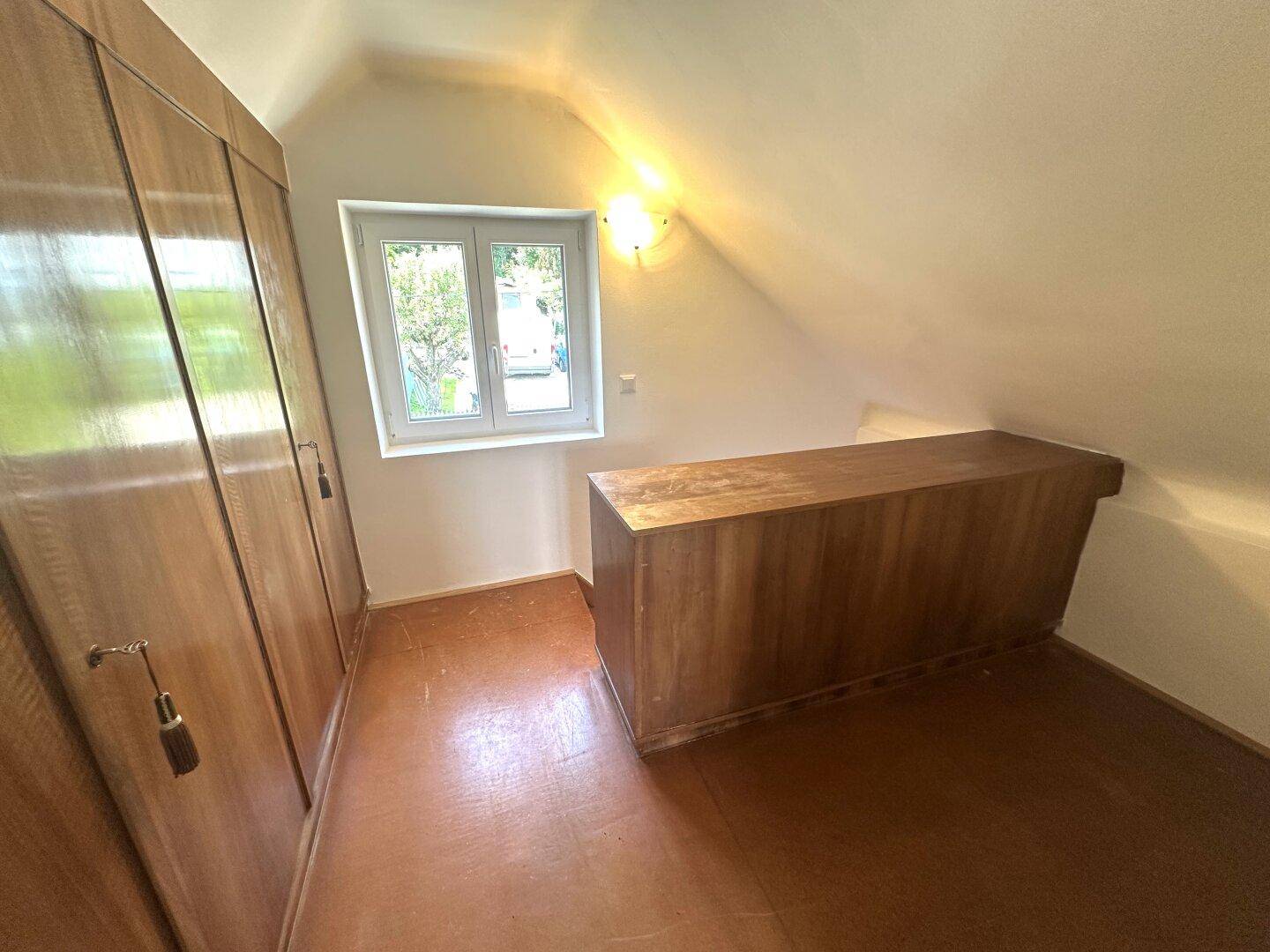 Dachgeschoss-Schlafzimmer mit Einbauschränken aus Holz und Fenster.