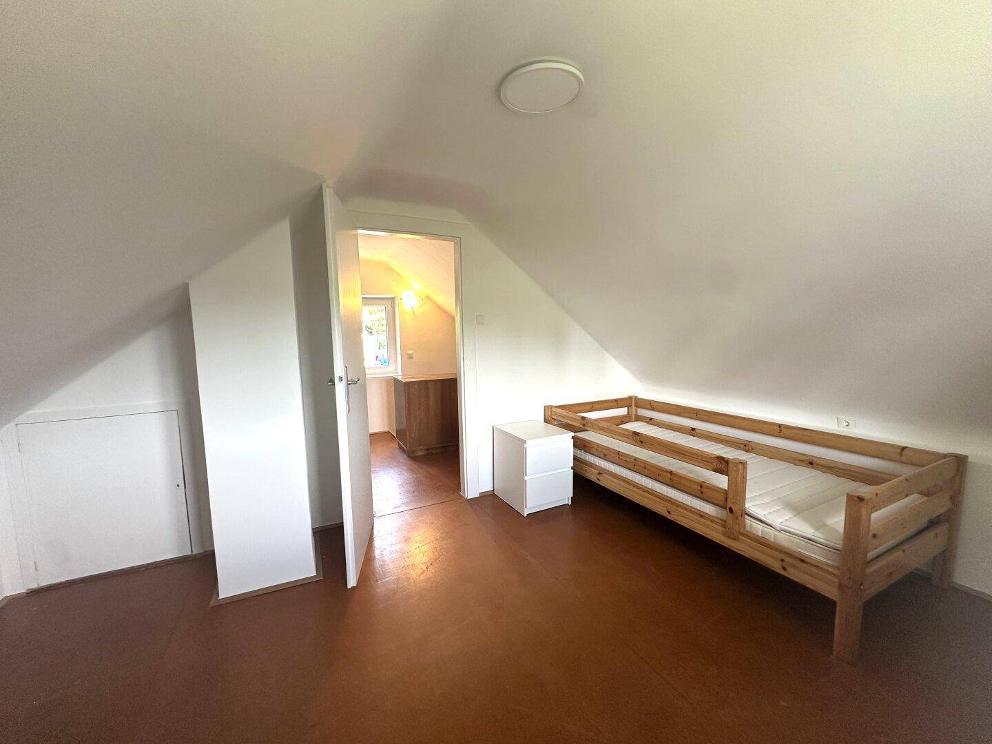 Dachgeschoss-Schlafzimmer mit Einzelbett und offener Tür zu einem weiteren Raum.