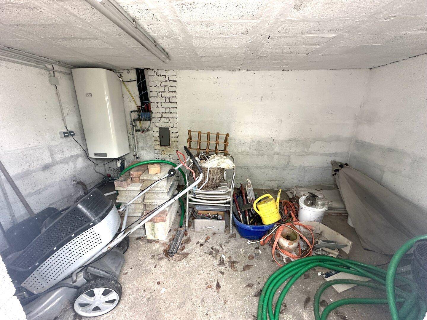 Kellerraum mit Betonwänden, Warmwasserbereiter und verschiedenen Werkzeugen.