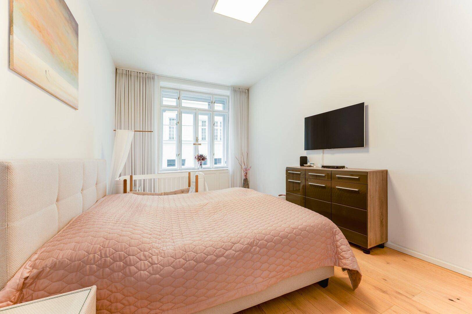 Helles Schlafzimmer mit großem Bett, Holzboden und einem Fenster mit Blick auf die Straße.