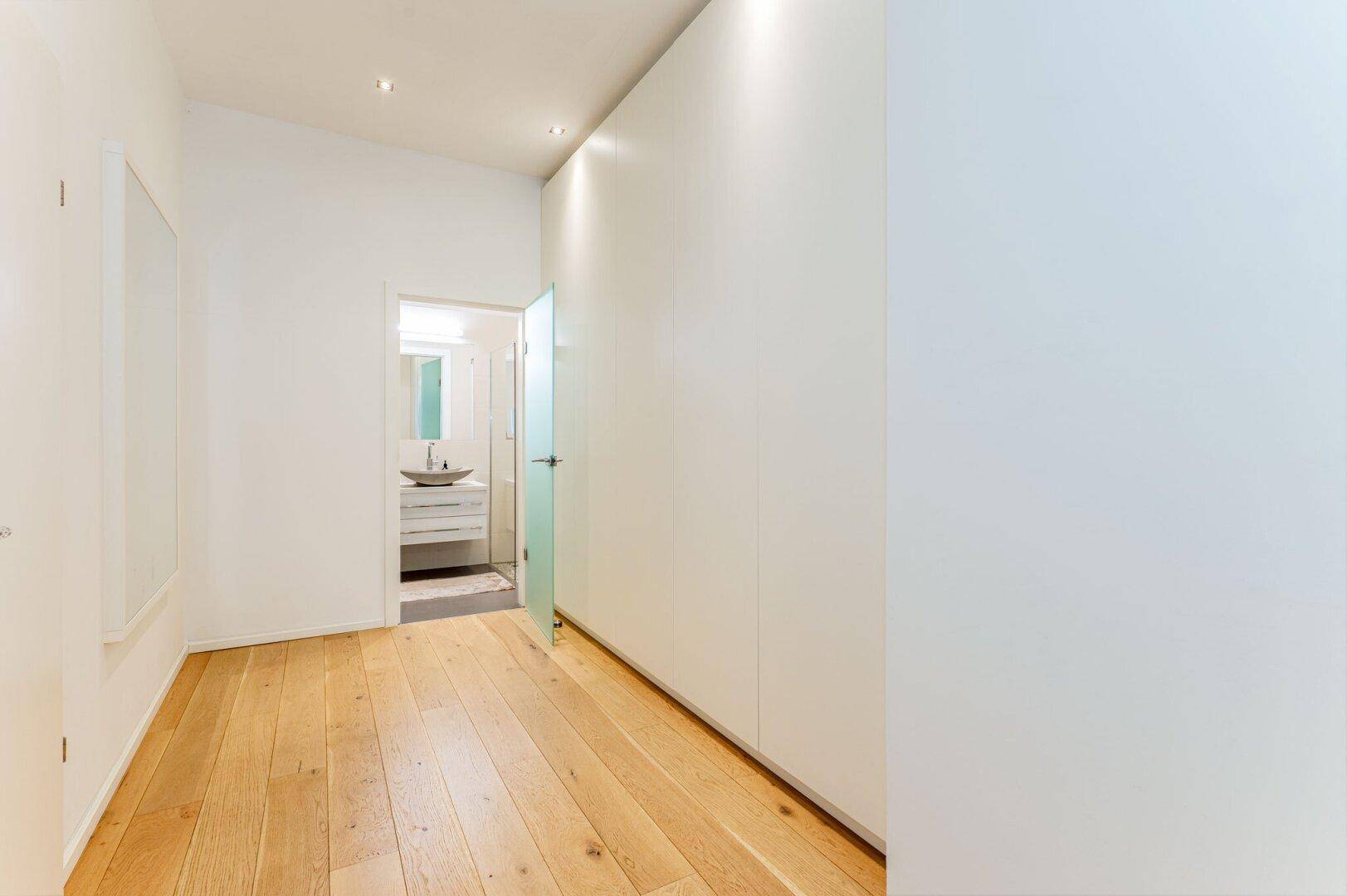 Heller Flur mit Holzboden und Einbauschränken, der zu einem modernen Badezimmer führt.