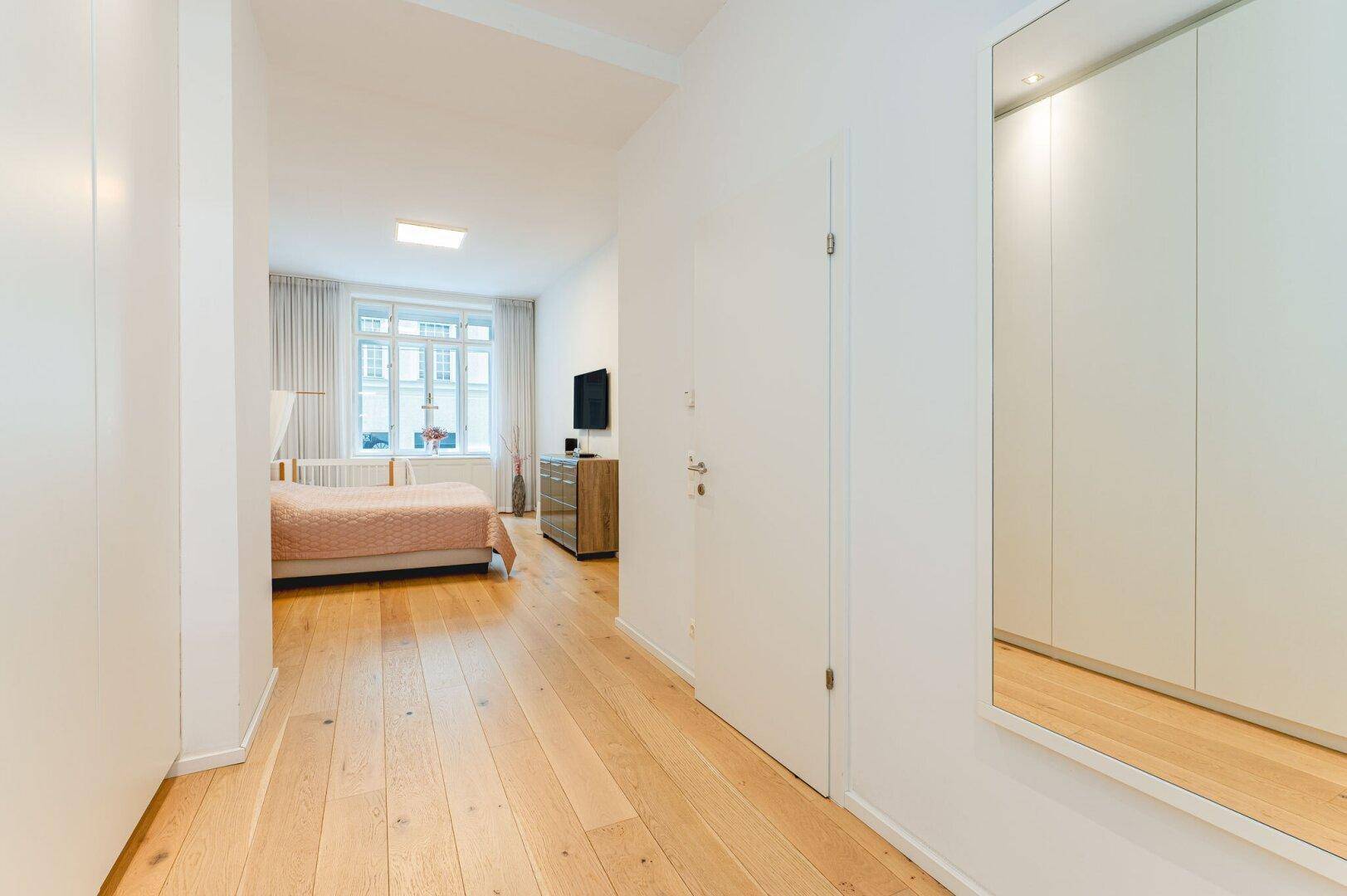 Langer, heller Flur mit Holzboden und Einbauschränken, der zum Schlafzimmer führt.