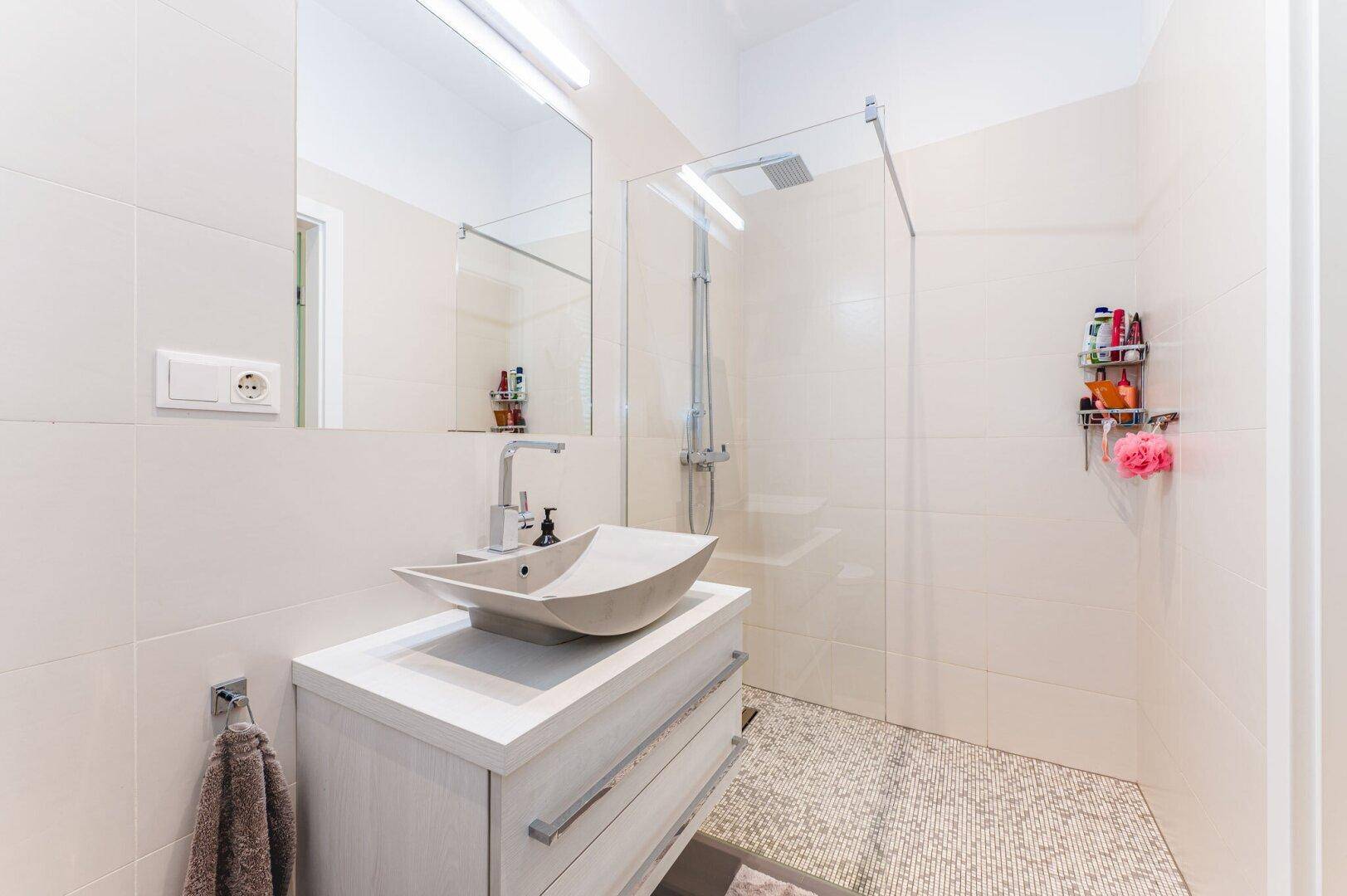 Modernes Badezimmer mit begehbarer Dusche, hellem Waschtisch und großen Fliesen.