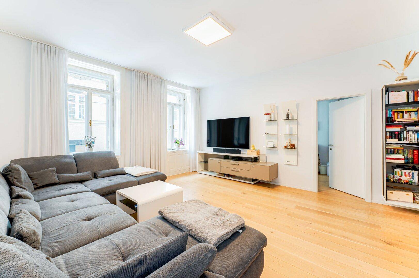 Geräumiges Wohnzimmer mit großem Ecksofa, Holzboden und großen Fenstern für viel Licht.