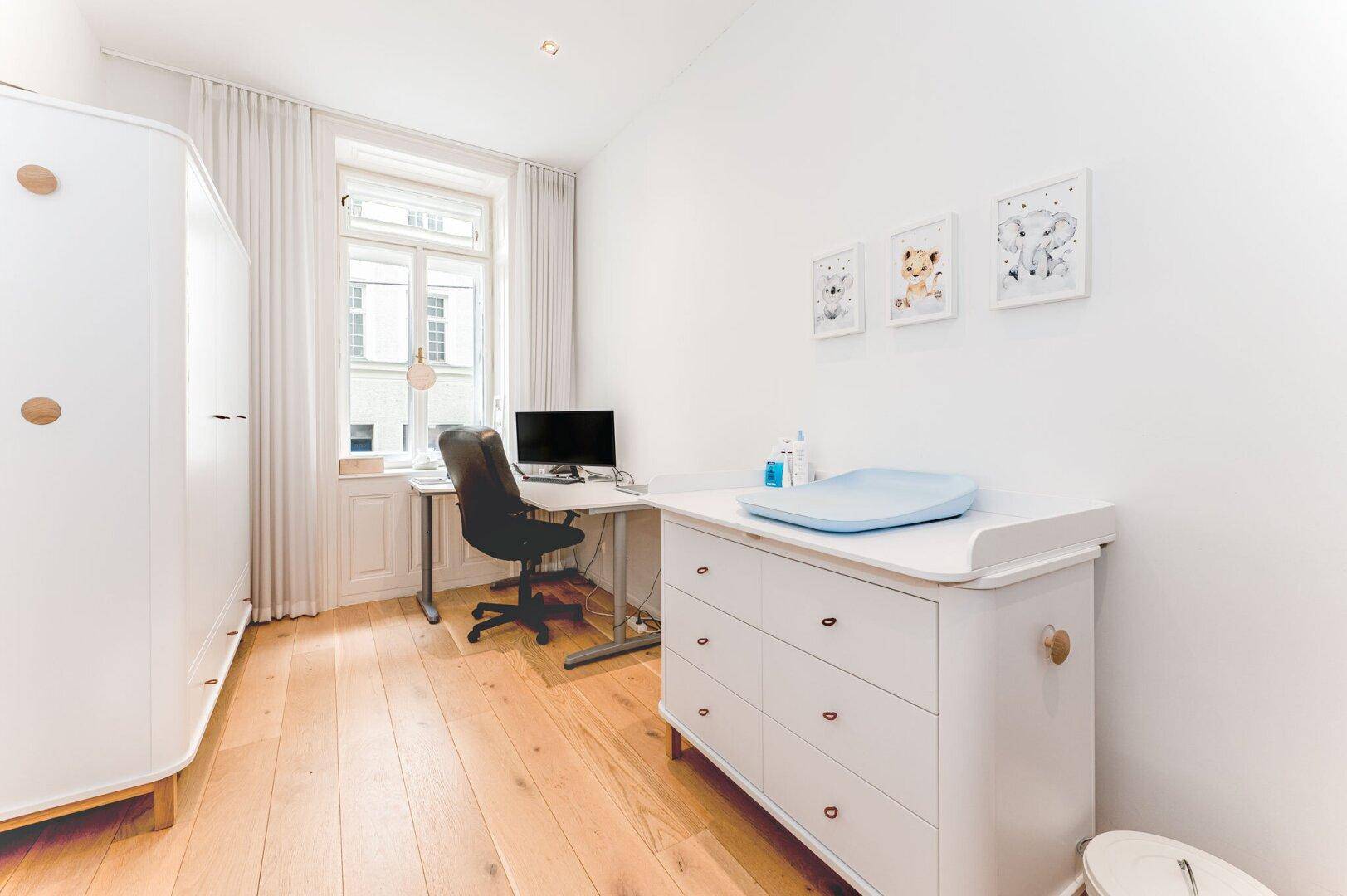 Helles Arbeitszimmer mit Schreibtisch, Schrank und Wickelkommode, ideal als Kinder- oder Gästezimmer.