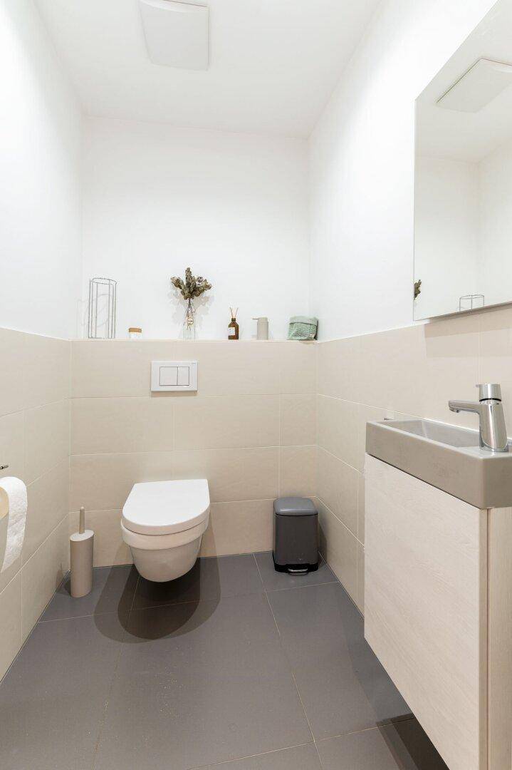 Modernes Gäste-WC mit wandhängender Toilette, kleinem Waschbecken und Spiegel.