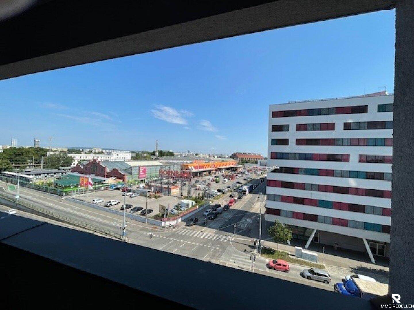 Blick von der Loggia auf eine belebte Straße, Parkplätze und umliegende Gebäude.
