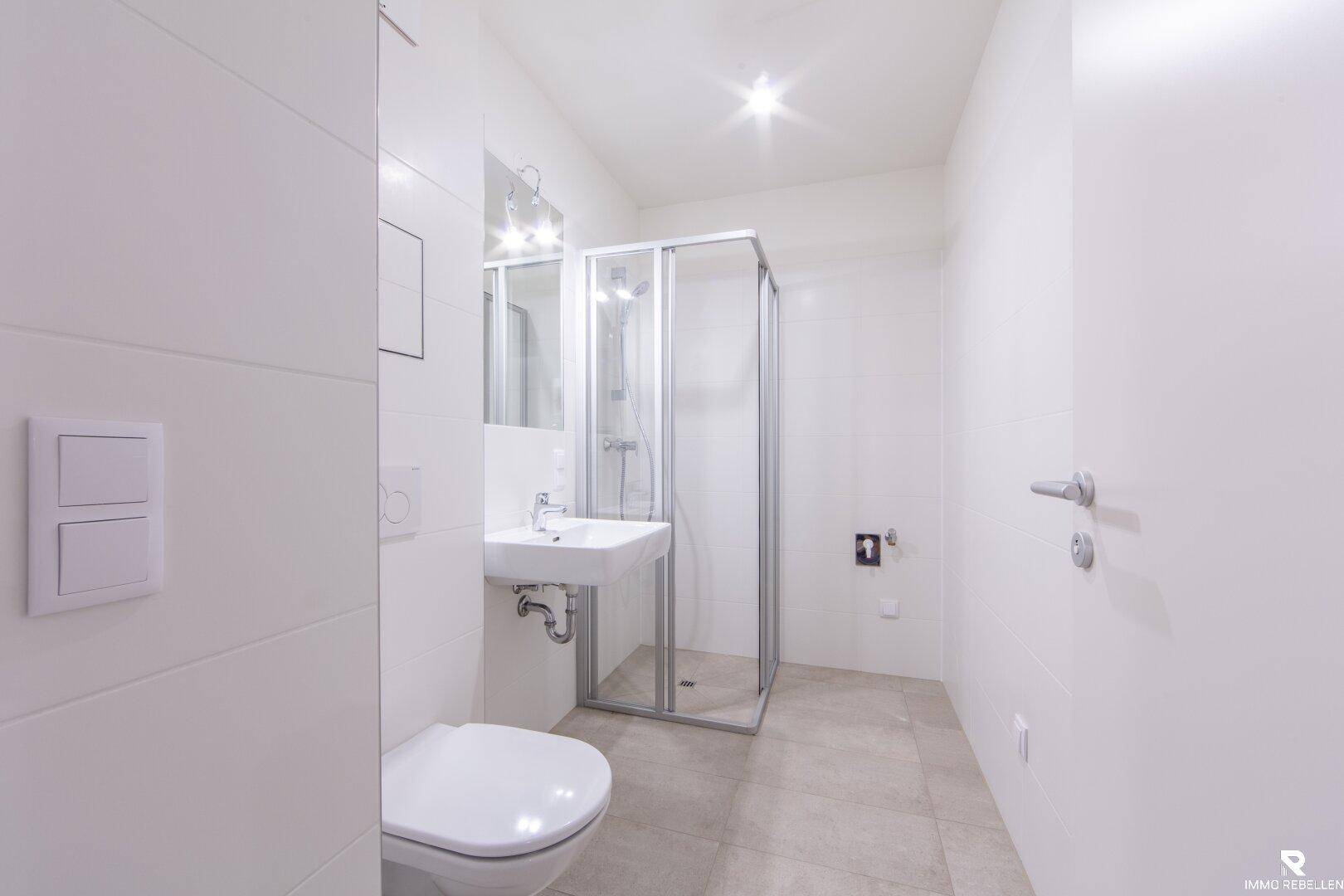 Modernes Badezimmer mit Duschkabine, wandhängendem WC und hellem Fliesenboden.