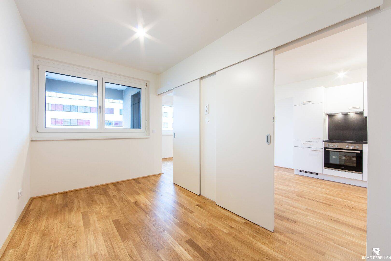 Helles Zimmer mit Schiebetüren zum Wohnbereich und Fenster mit Blick nach draußen.