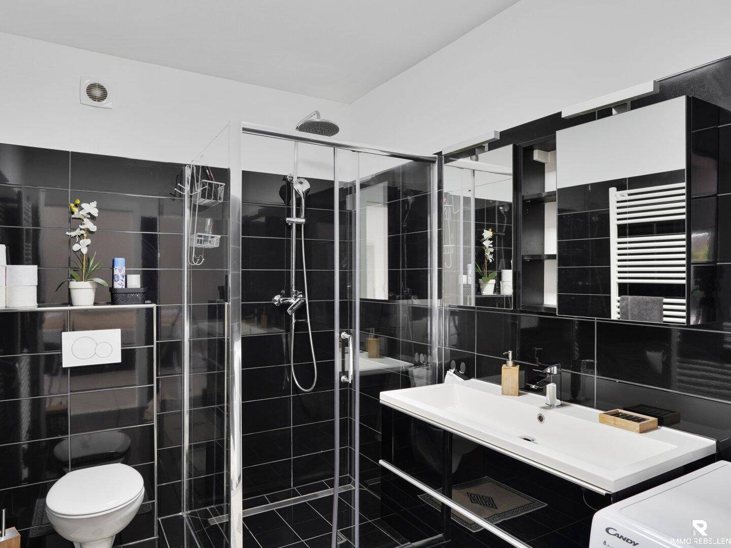 Modernes Badezimmer mit schwarzem Fliesenboden, Dusche und integrierter Waschmaschine.