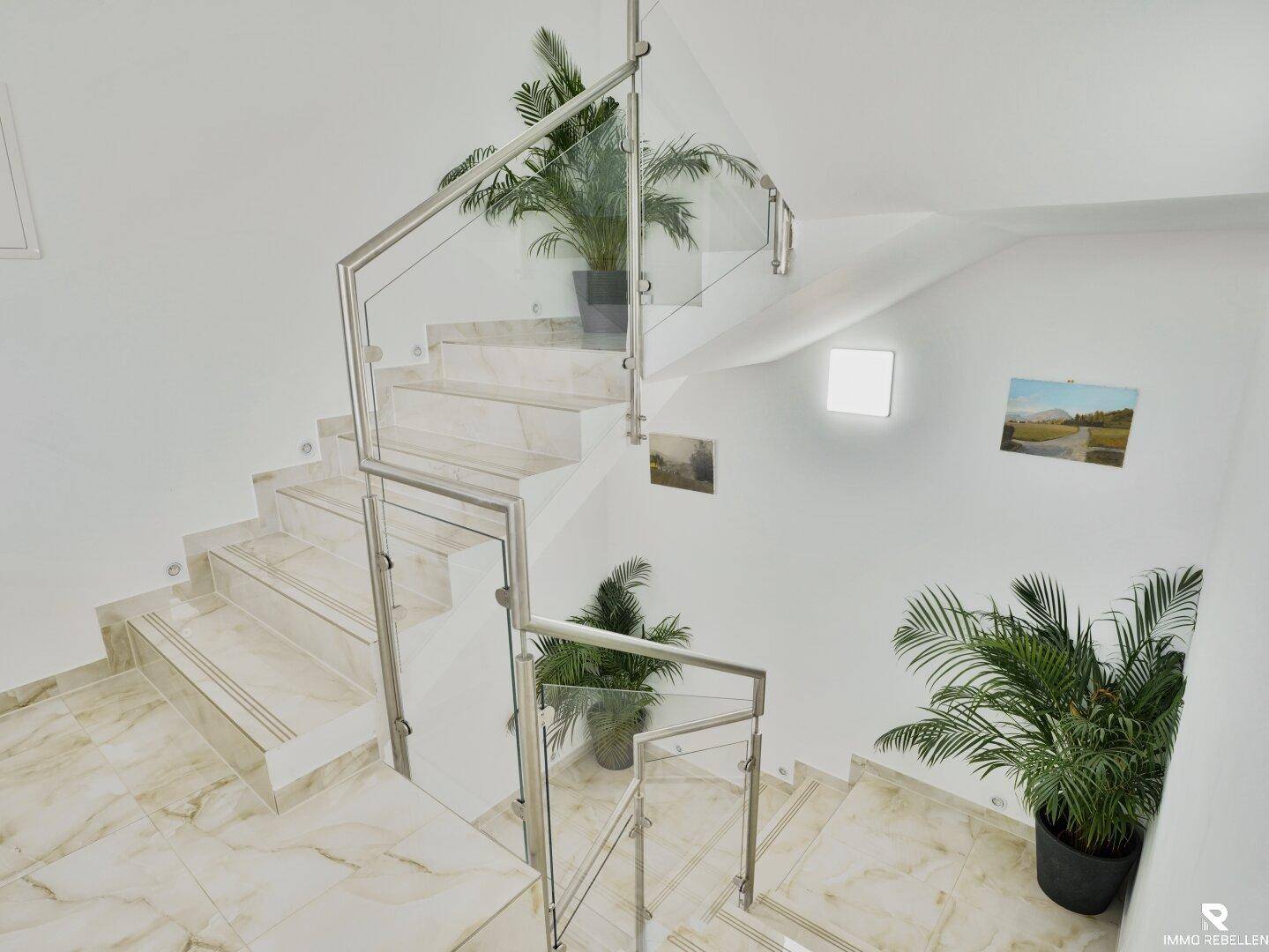 Elegantes Treppenhaus mit Marmorstufen, Glasgeländer und dekorativen Pflanzen.