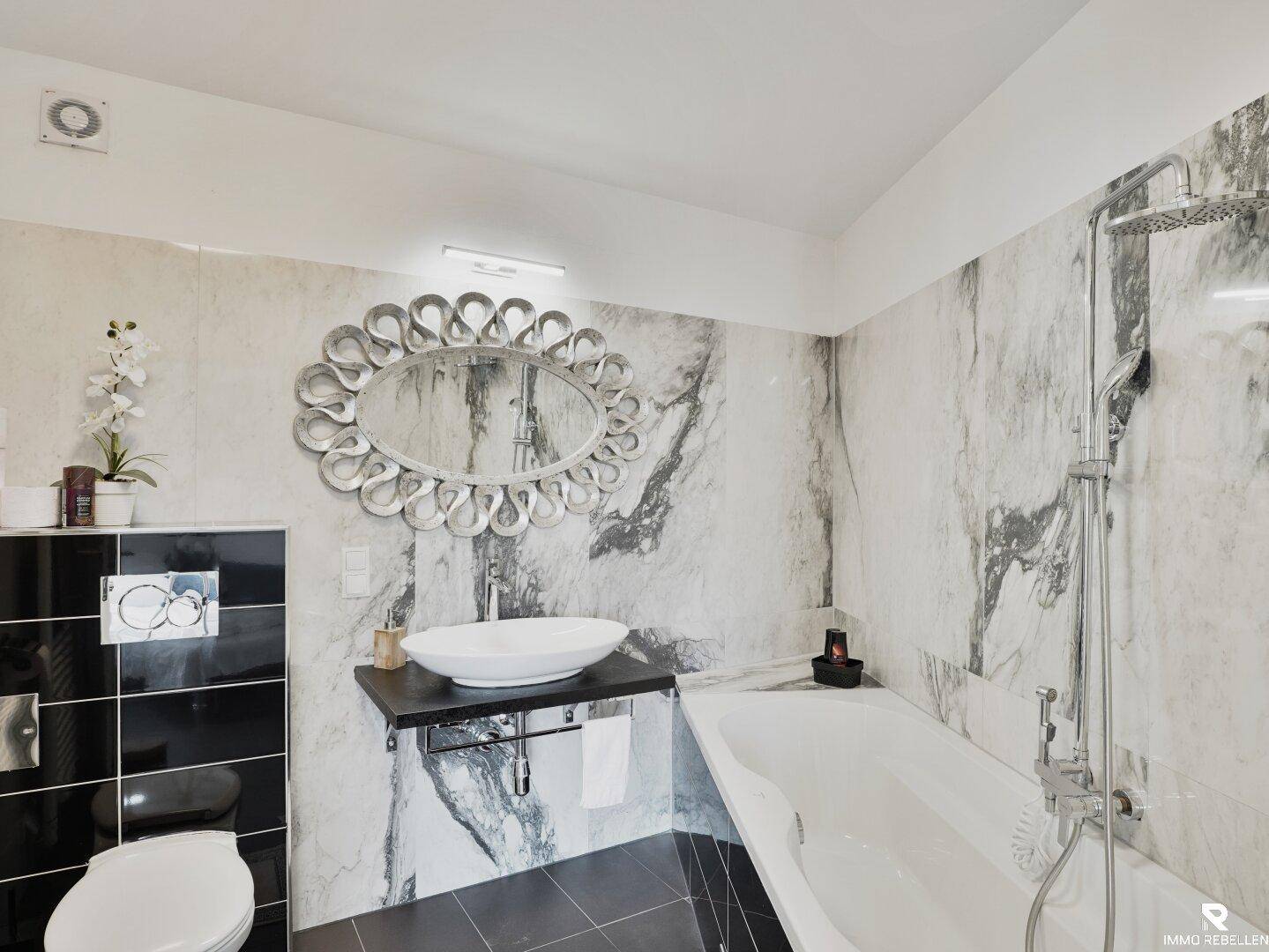 Modernes Badezimmer mit Badewanne, ovalem Spiegel und Marmor-Effekt-Fliesen.