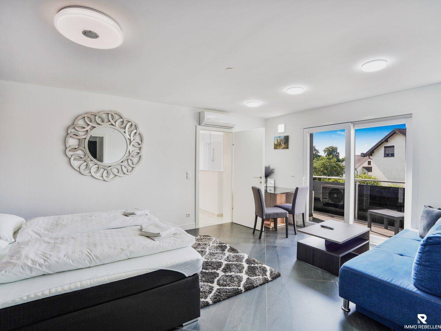 Lichtdurchflutetes Schlafzimmer mit Bett, Sofa und direktem Zugang zum Balkon.