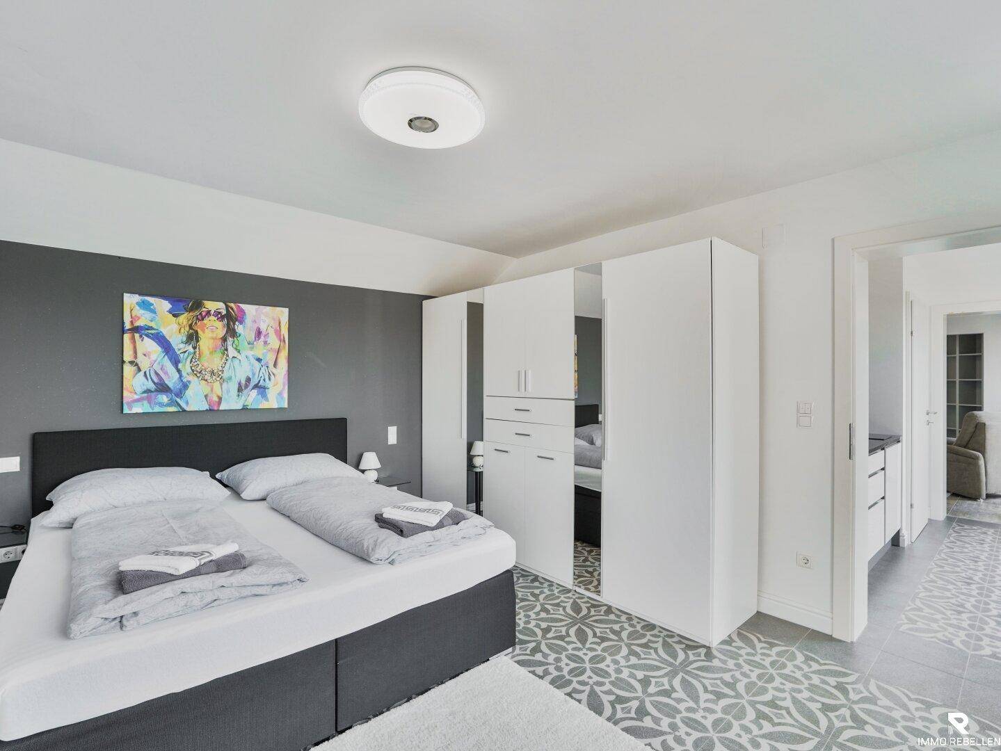 Schlafzimmer mit Doppelbett, moderner Kunst und weißem Einbauschrank mit Spiegeltüren.