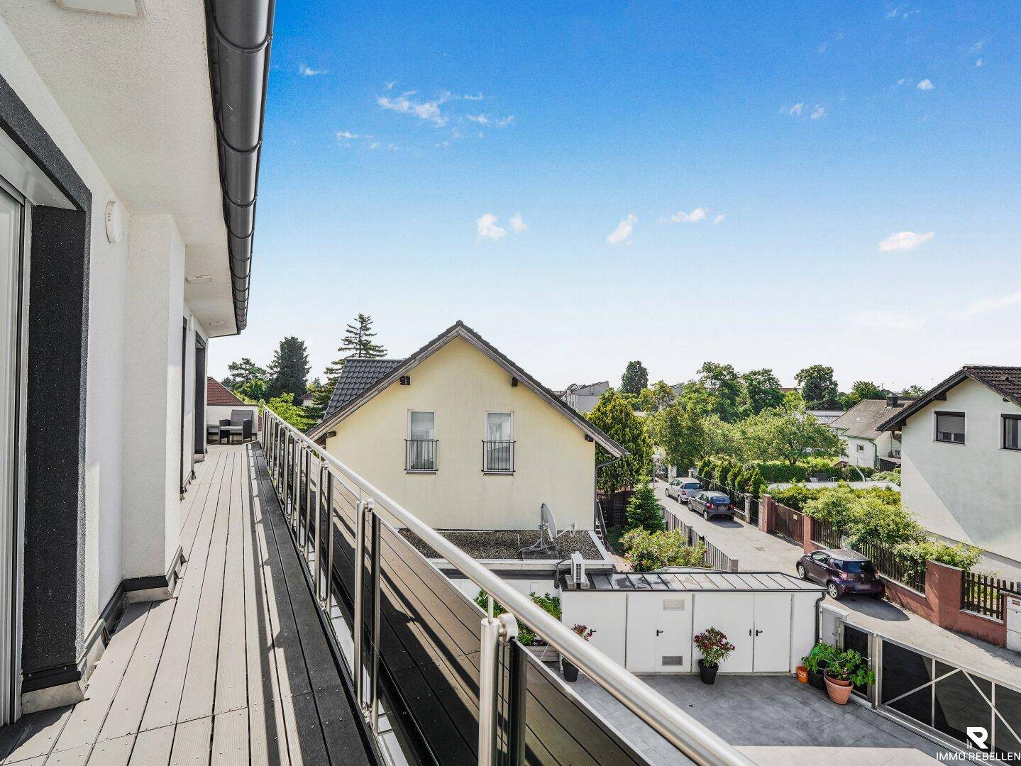 Langer Balkon mit Holzboden und Blick auf die Nachbarschaft und die Straße.