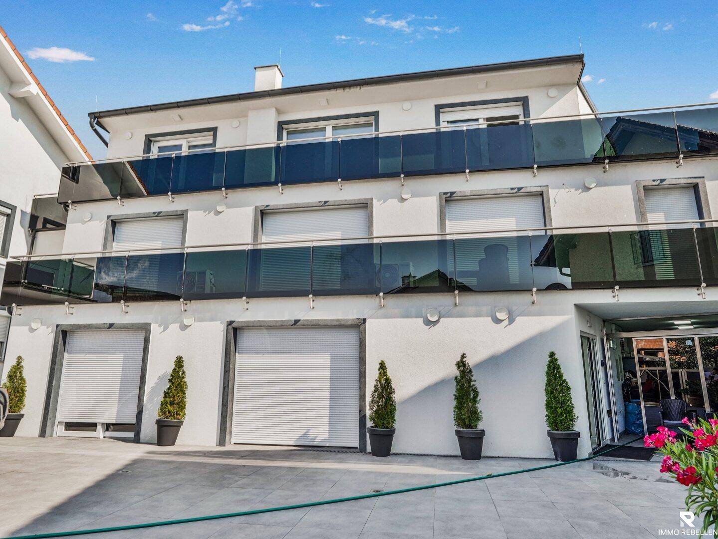 Weiße Gebäudefassade mit mehreren Garagentoren und Balkonen mit Glasgeländer.