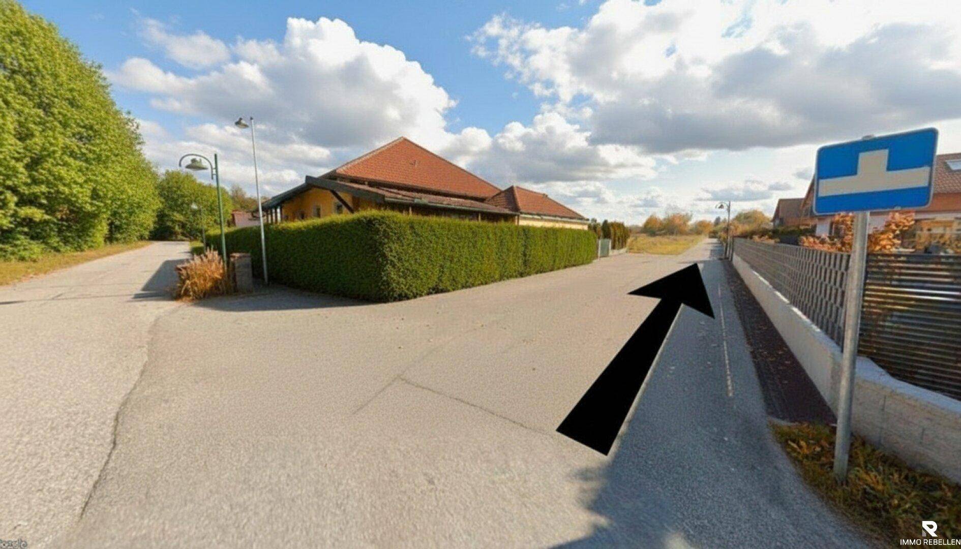 Blick auf eine ruhige Wohnstraße mit einem modernen Haus, Hecke und Verkehrsschild.