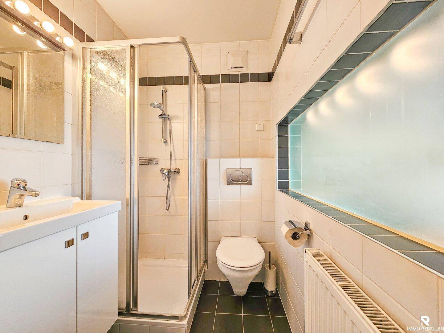 Gefliestes Badezimmer mit Duschkabine, wandhängender Toilette und einem einzelnen Waschbecken.