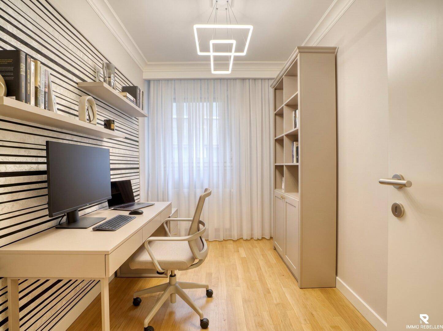 Helles Arbeitszimmer mit Schreibtisch, Bücherregal und gestreifter Tapete.