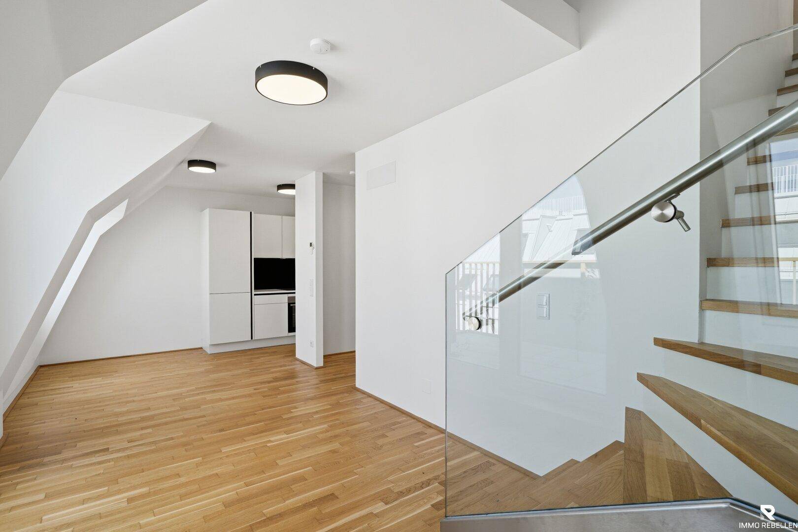 Offener Wohnbereich mit Holzboden, moderner Treppe und integrierter Küchenzeile.