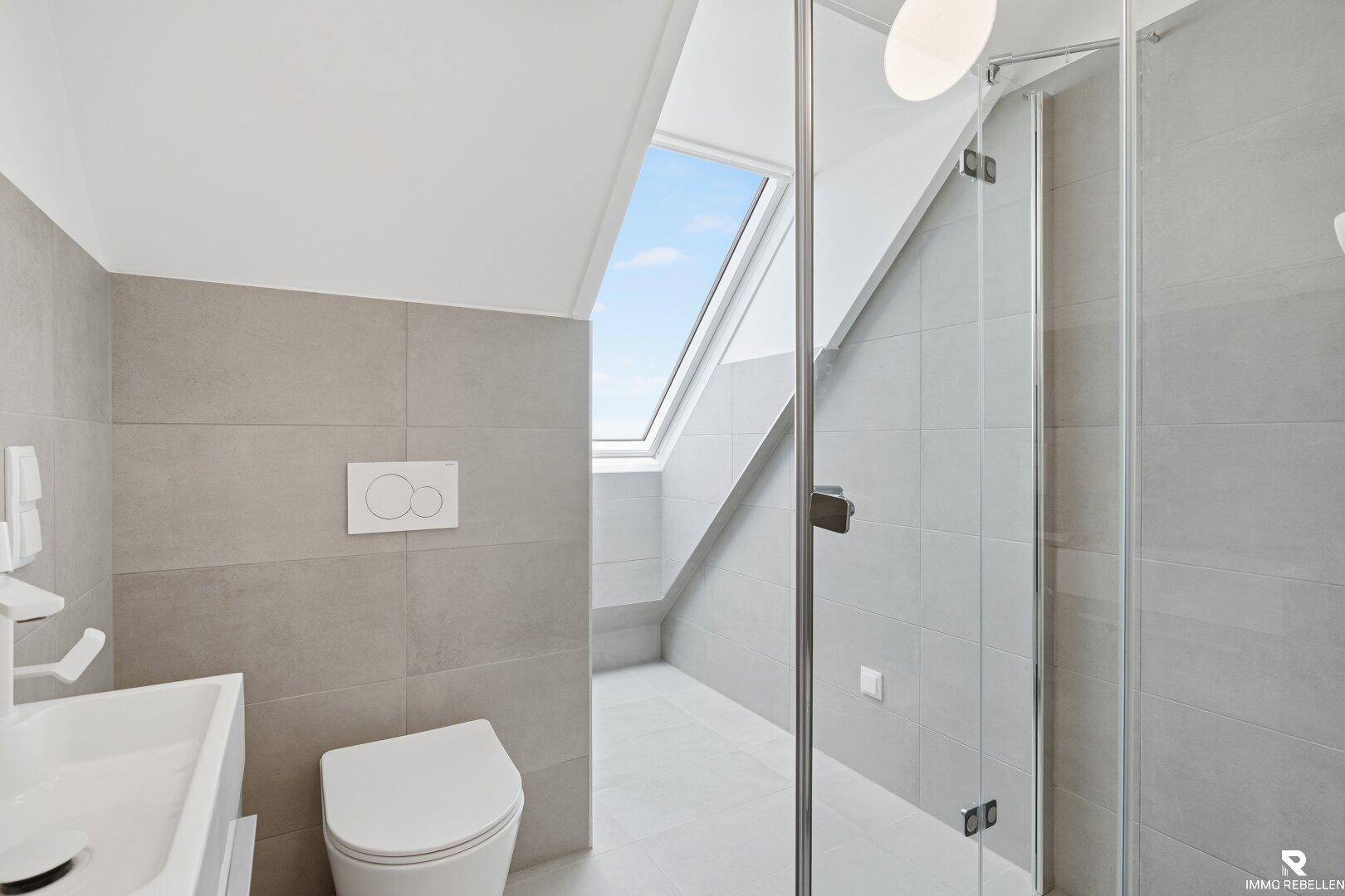 Modernes Badezimmer mit grauen Fliesen, Dusche, wandhängendem WC und Dachfenster.