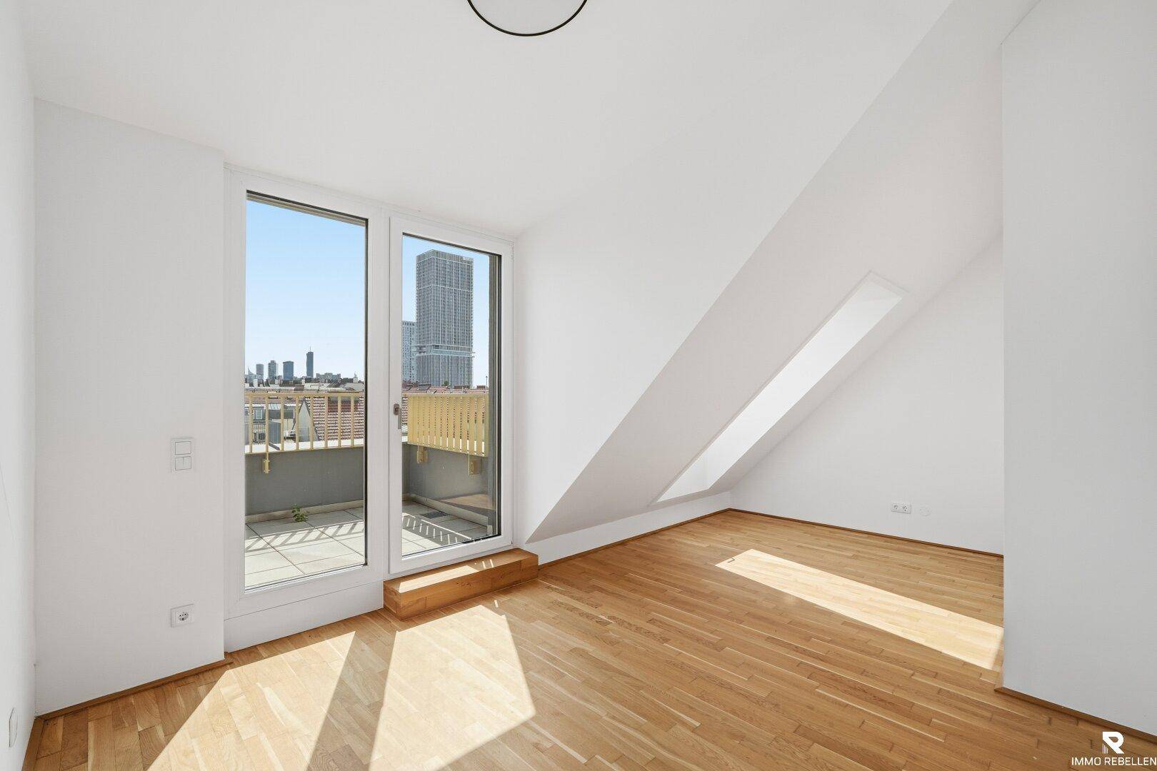 Helles Schlafzimmer mit Holzboden, Zugang zur Terrasse und weitem Blick über die Stadt.