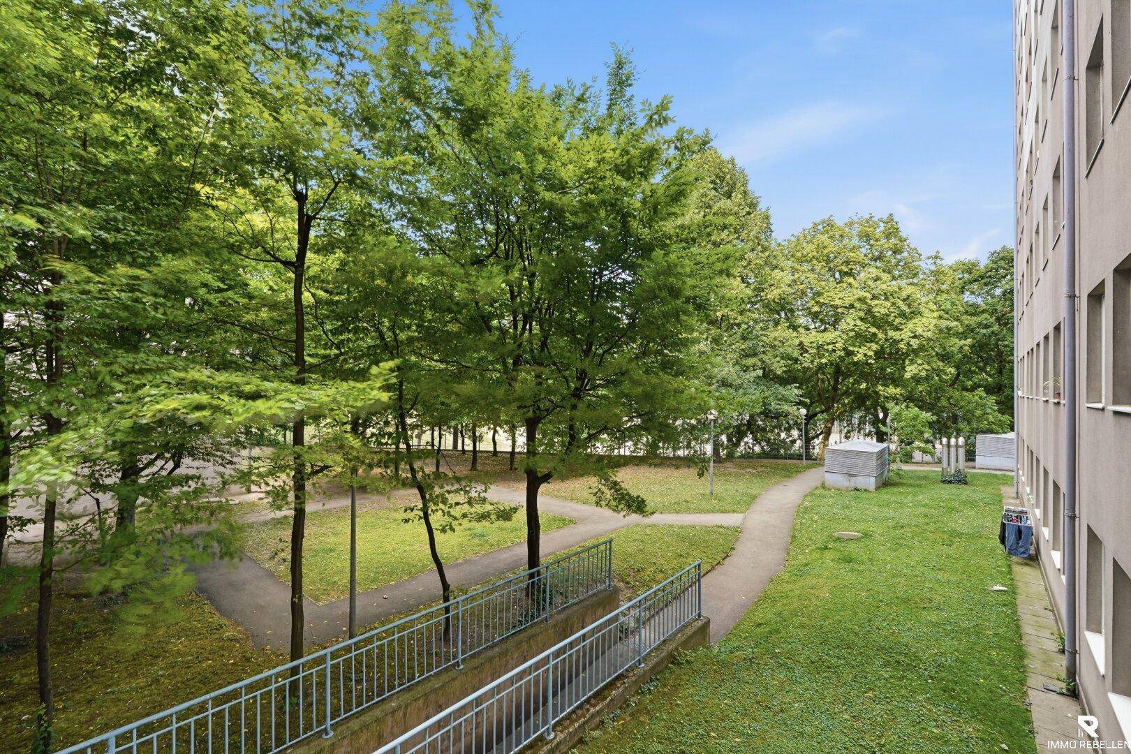 Blick auf den grünen Innenhof mit Bäumen und Gehwegen, ideal zur Erholung.