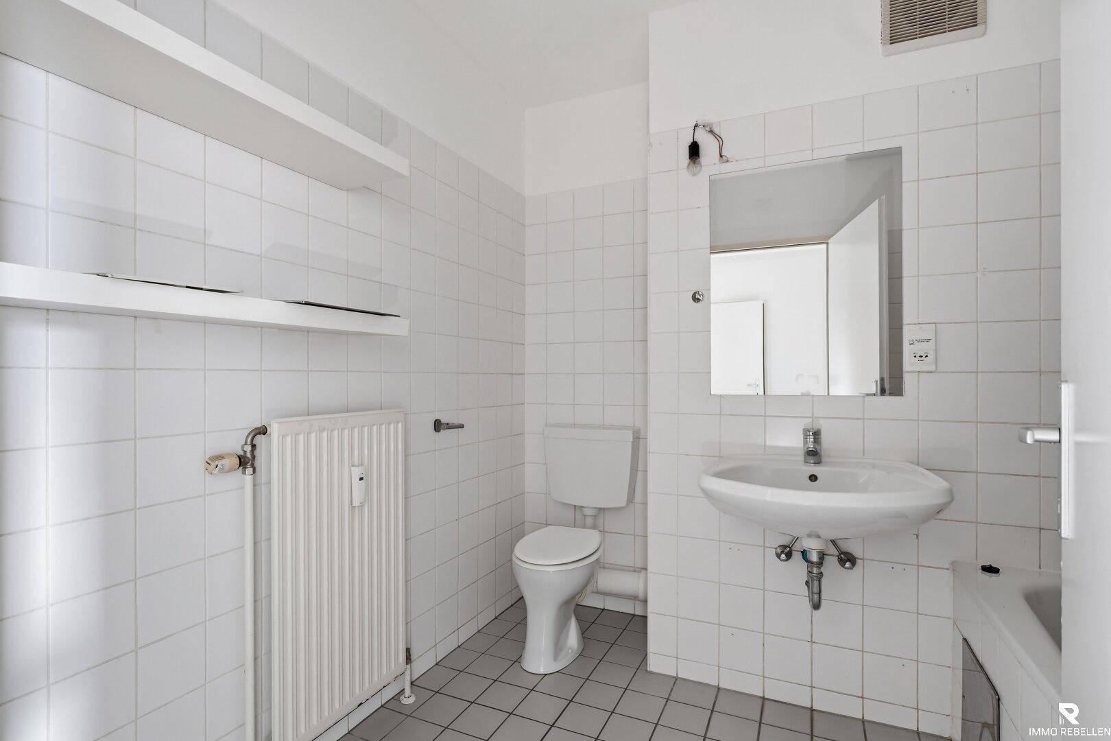 Helles Badezimmer mit weißen Fliesen, WC, Waschbecken und Heizkörper.