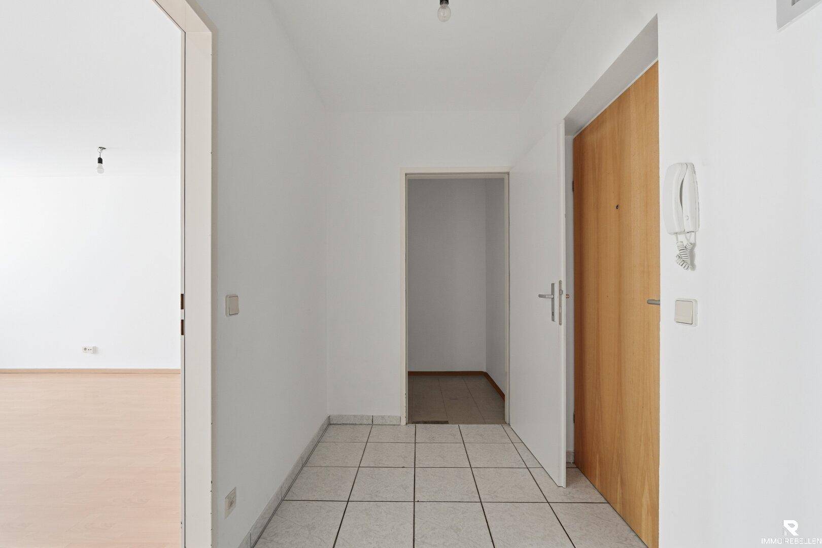 Eingangsbereich mit Fliesenboden, Holztür und Gegensprechanlage.