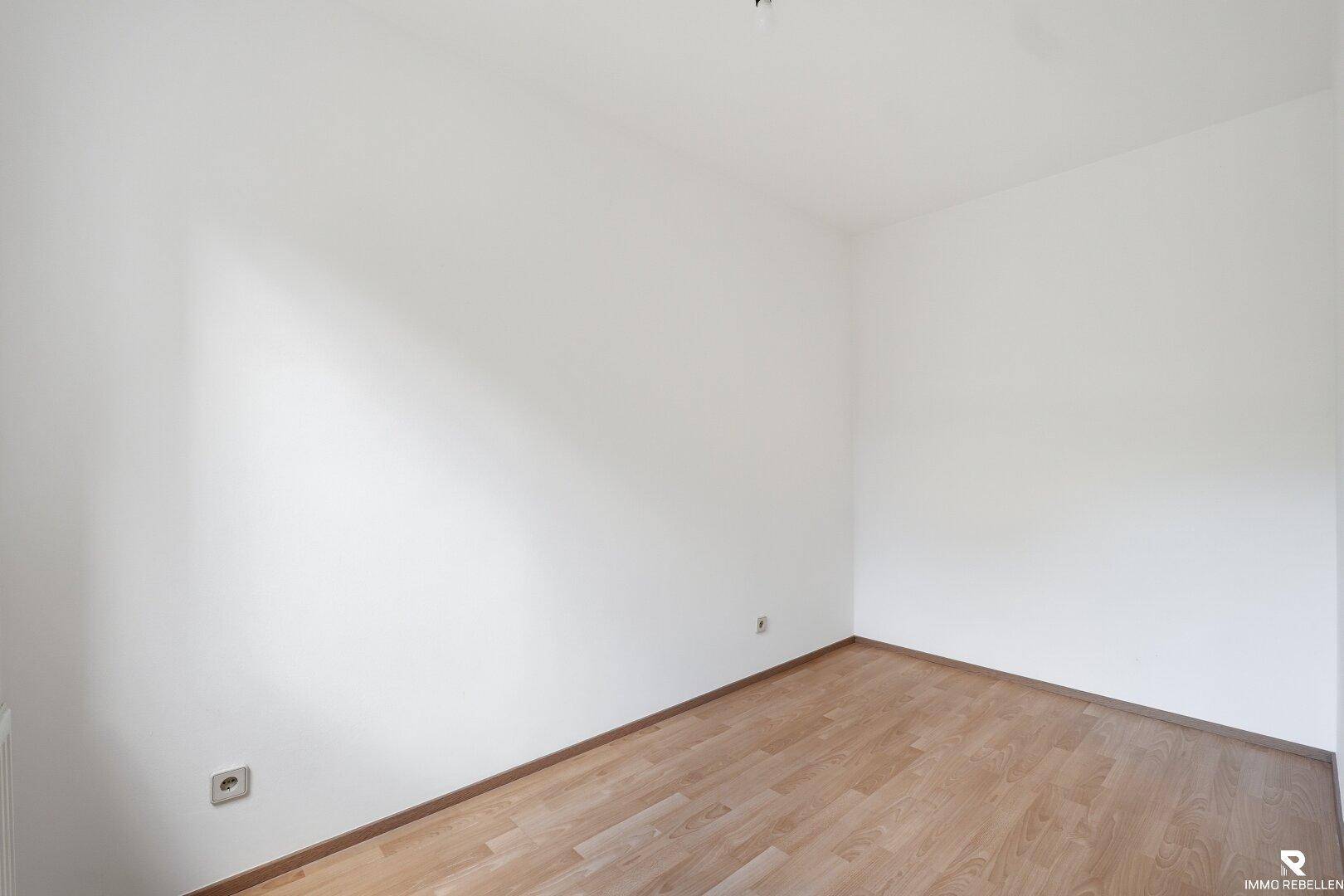 Leeres Schlafzimmer mit hellem Parkettboden und weißen Wänden.