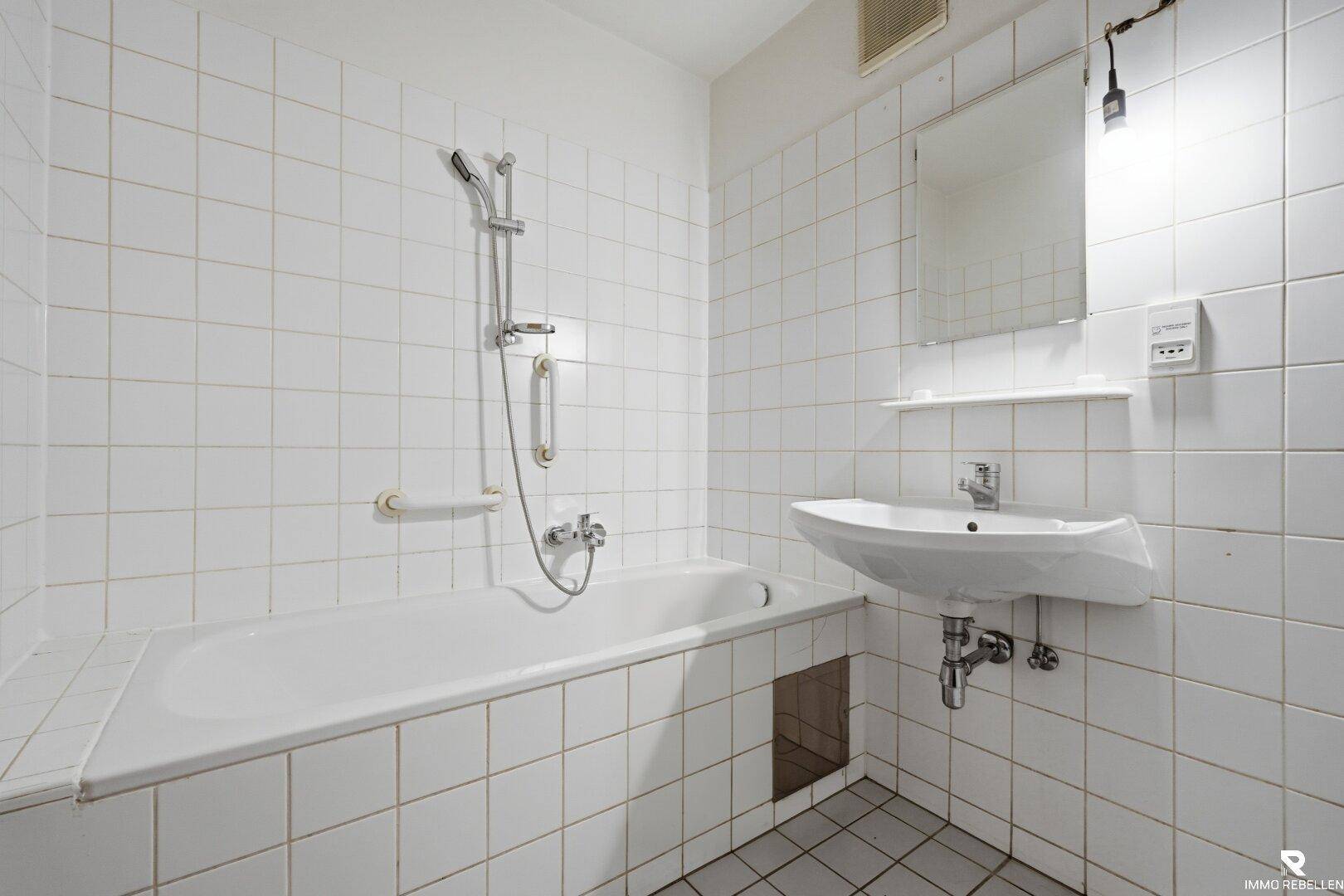 Gefliestes Badezimmer mit Badewanne, Duschfunktion und einem einzelnen Waschbecken.