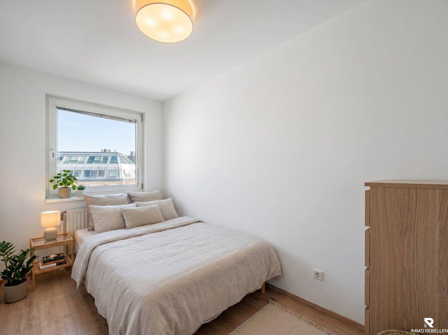 Gemütliches Schlafzimmer mit Holzboden, großem Fenster und einfacher, moderner Einrichtung.