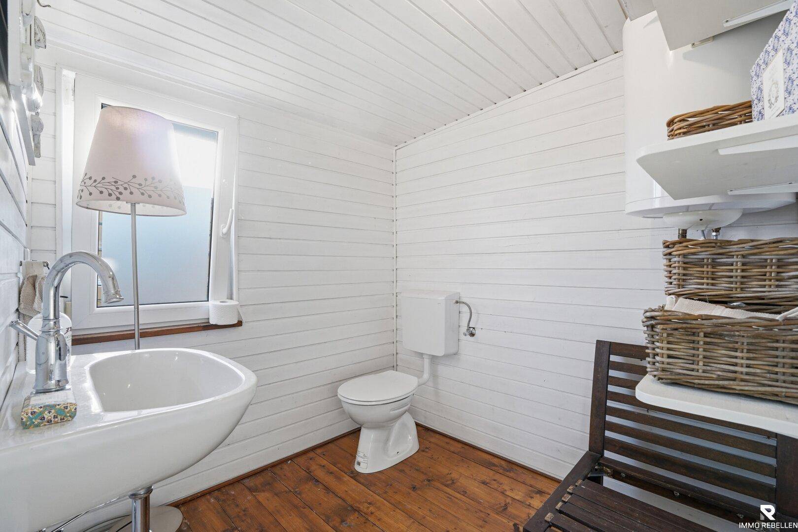 Kleines WC mit Waschbecken, Toilette und einem Fenster für natürliches Licht.