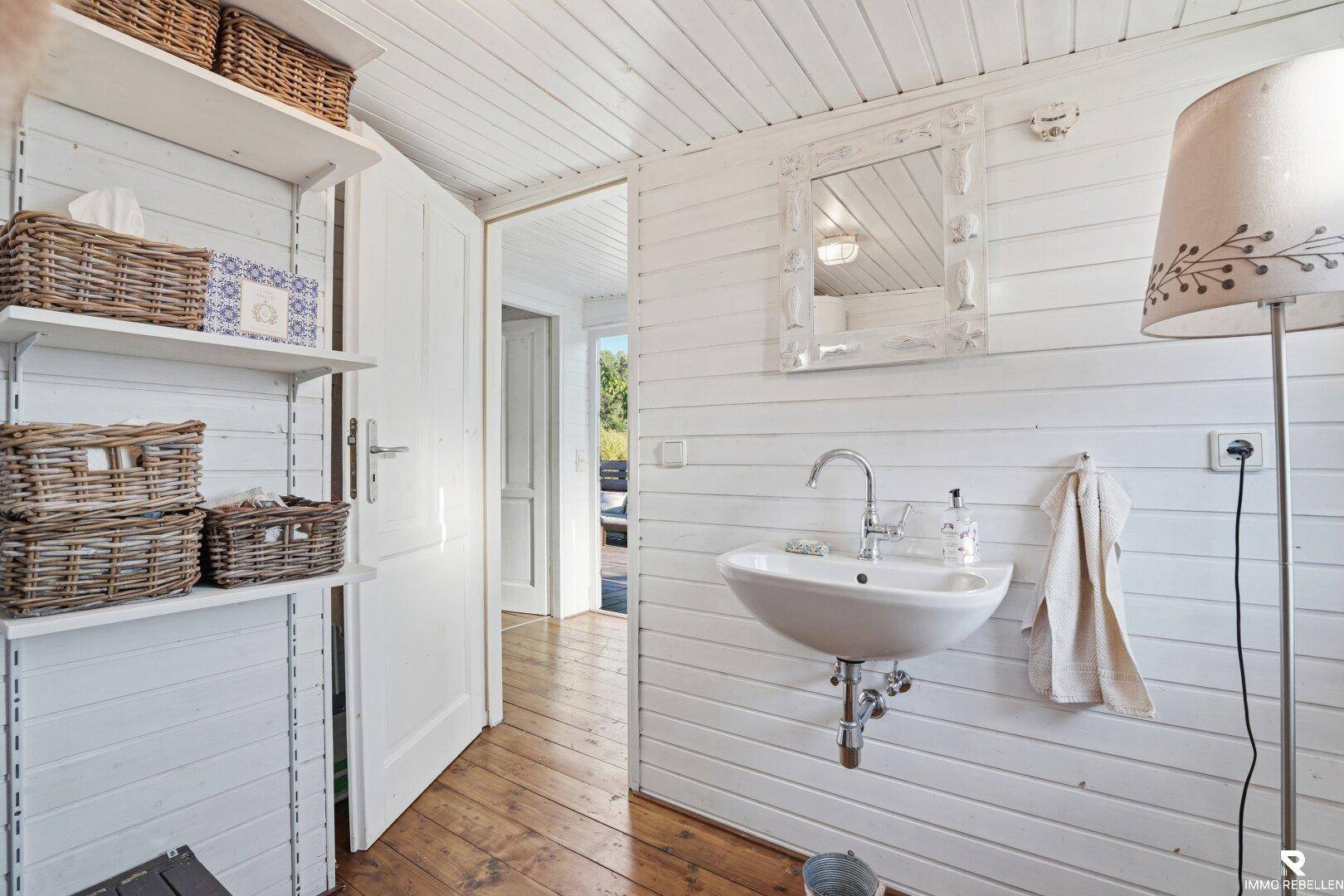 Helles WC mit Waschbecken, weißen Holzpaneelen und praktischen Regalen.