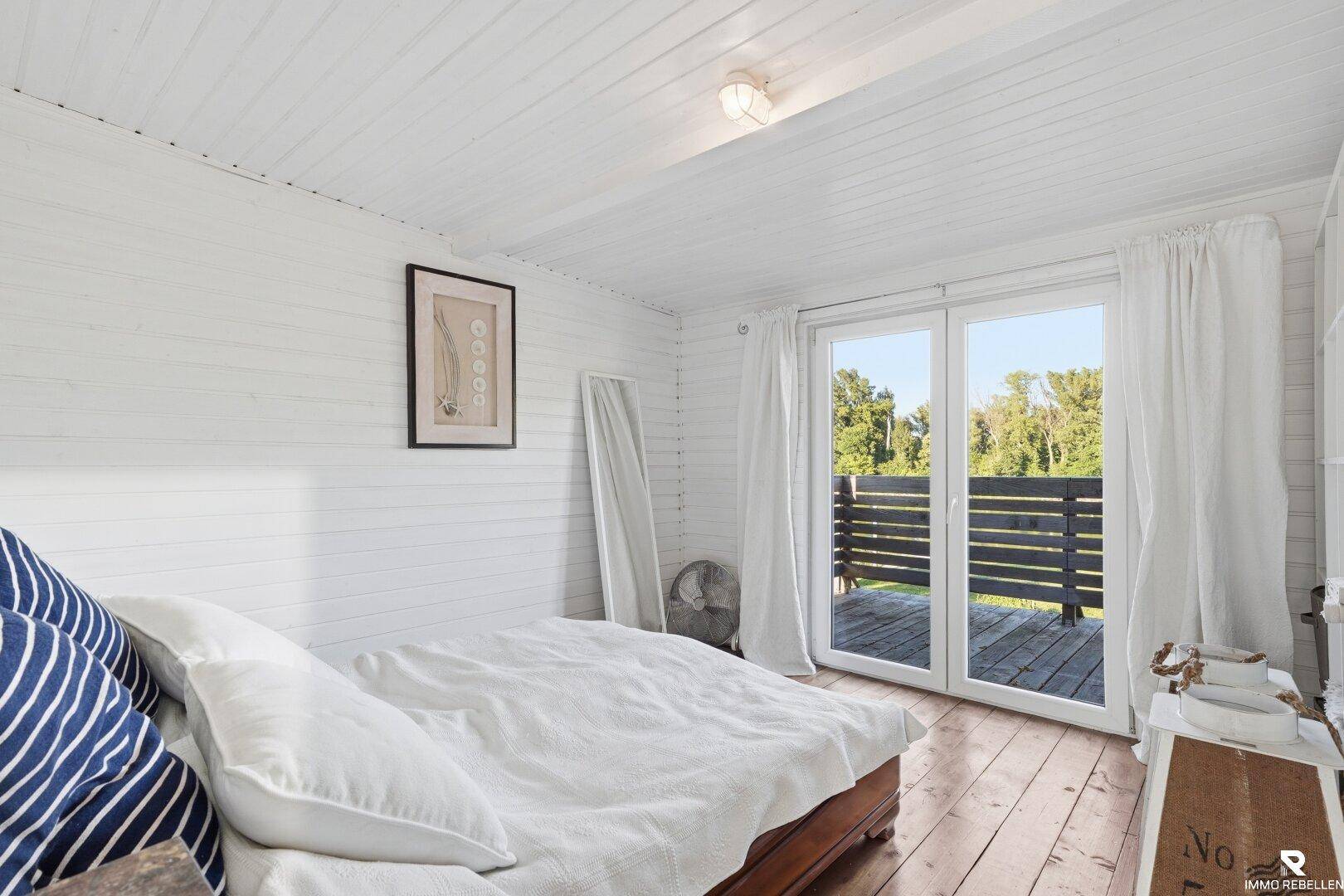 Helles Schlafzimmer mit Doppelbett, Holzboden und direktem Zugang zu einem Balkon.