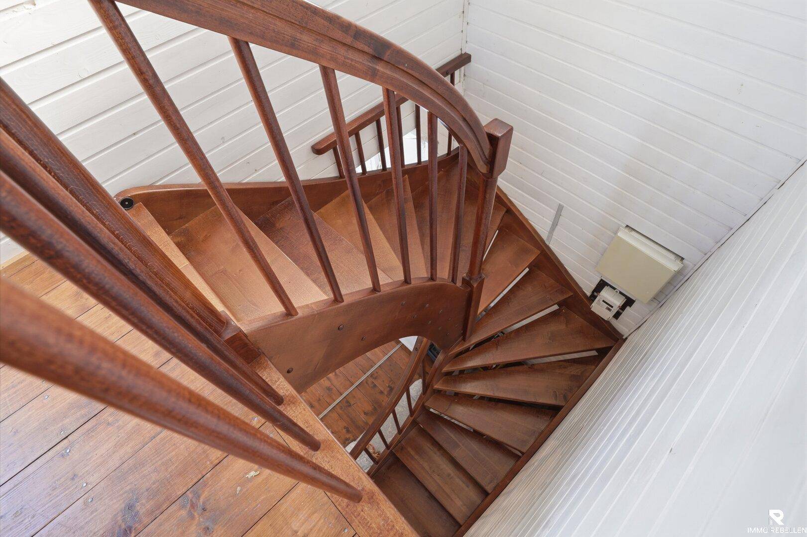 Elegante Holzwendeltreppe mit Geländer, die die verschiedenen Ebenen des Hauses verbindet.