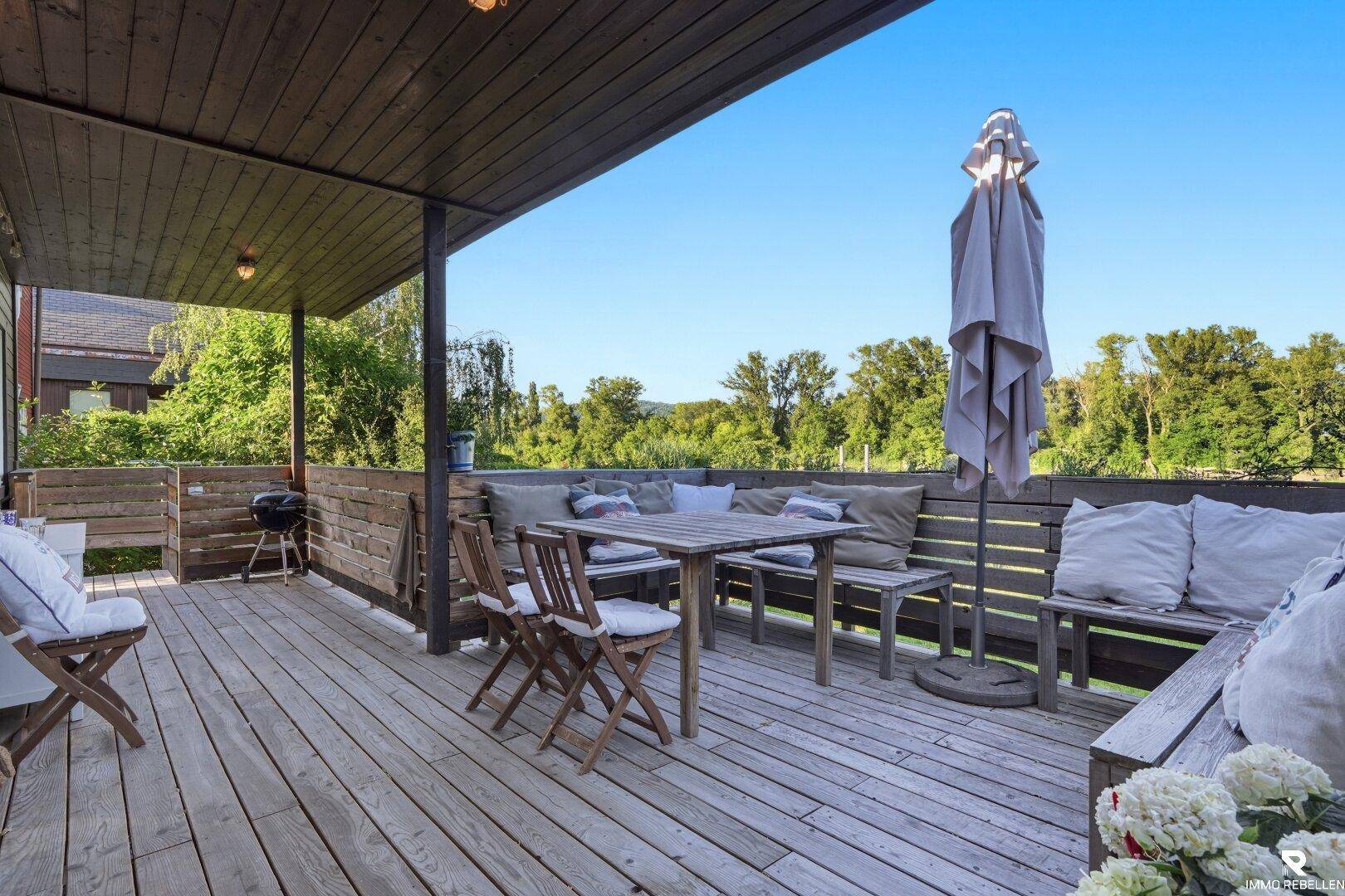 Geräumige Holzterrasse mit Sitzgelegenheiten, Grill und weitem Blick ins Grüne.